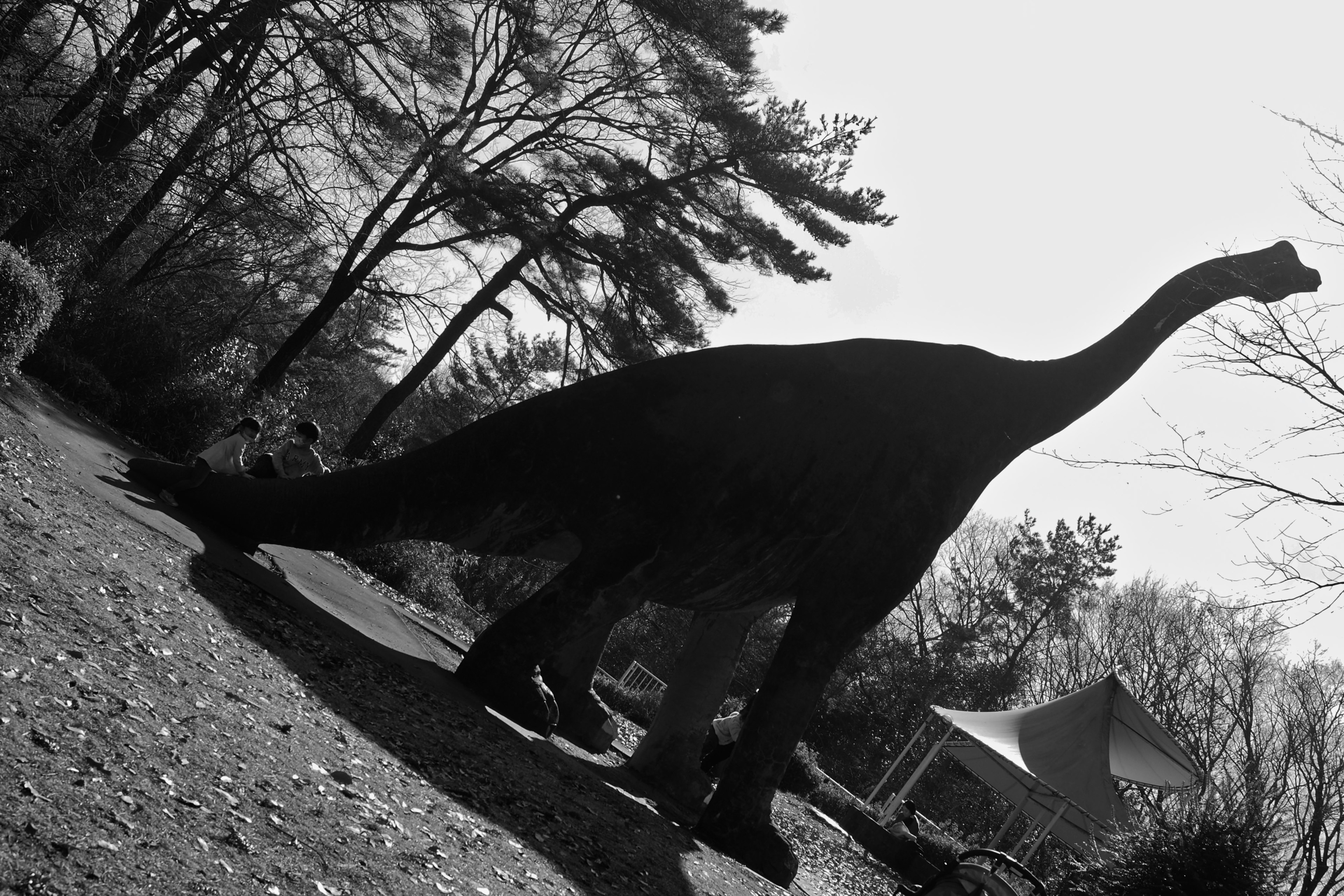 Silhouette of a dinosaur against a black and white background with trees and a structure in the vicinity