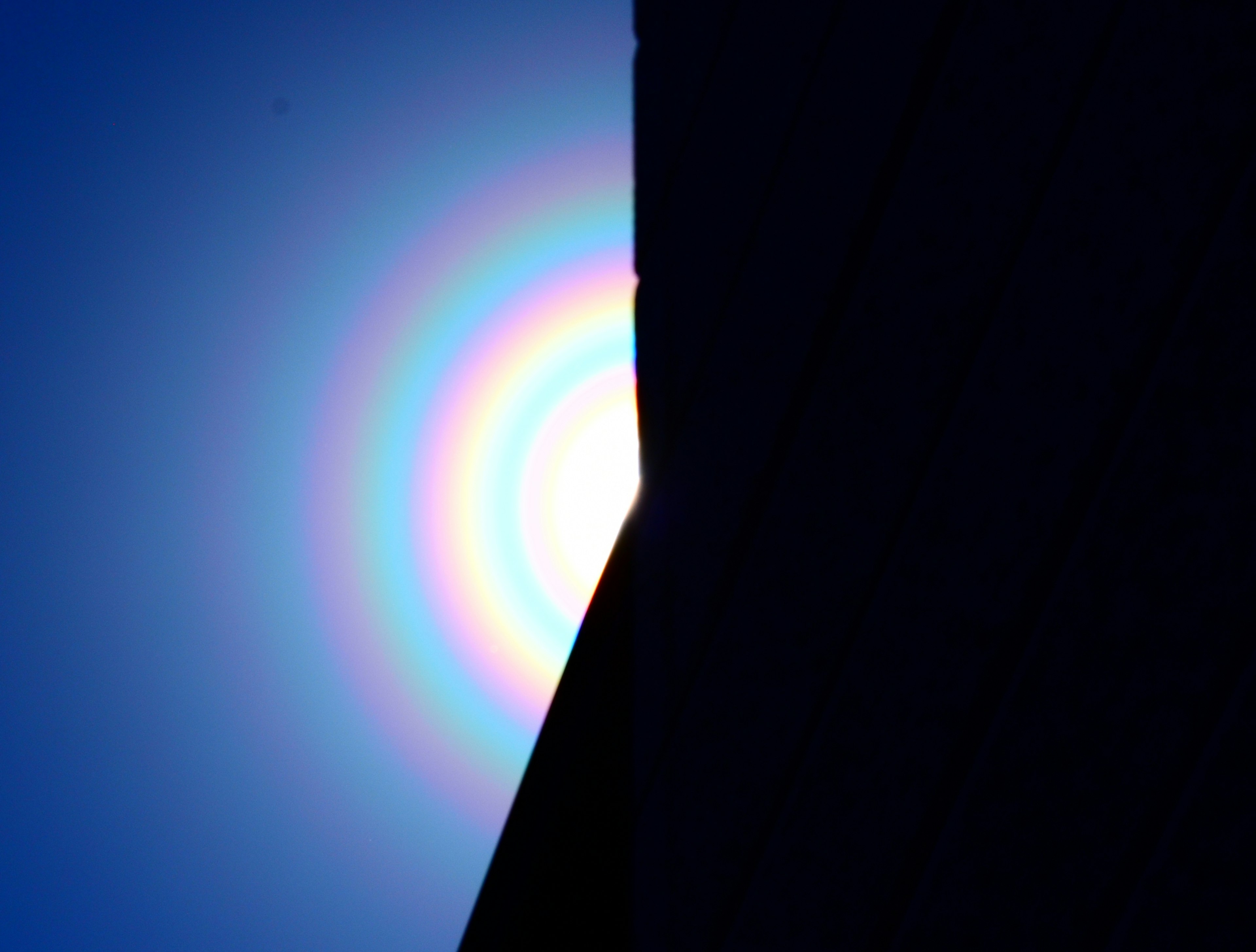 Contrast of a rainbow-colored circle against a blue sky and dark silhouette