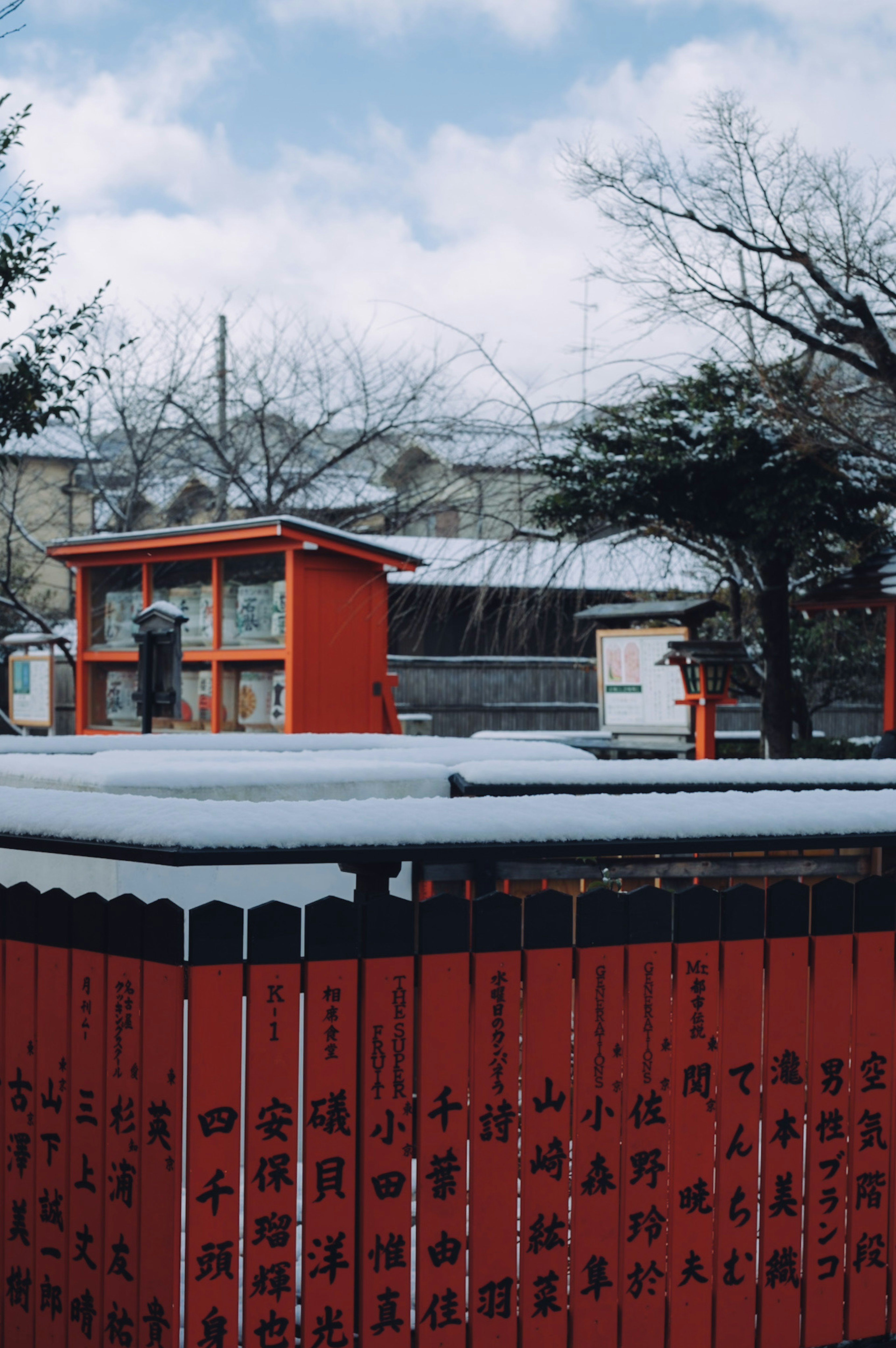 Winter scene with a snow-covered red fence and buildings in the background