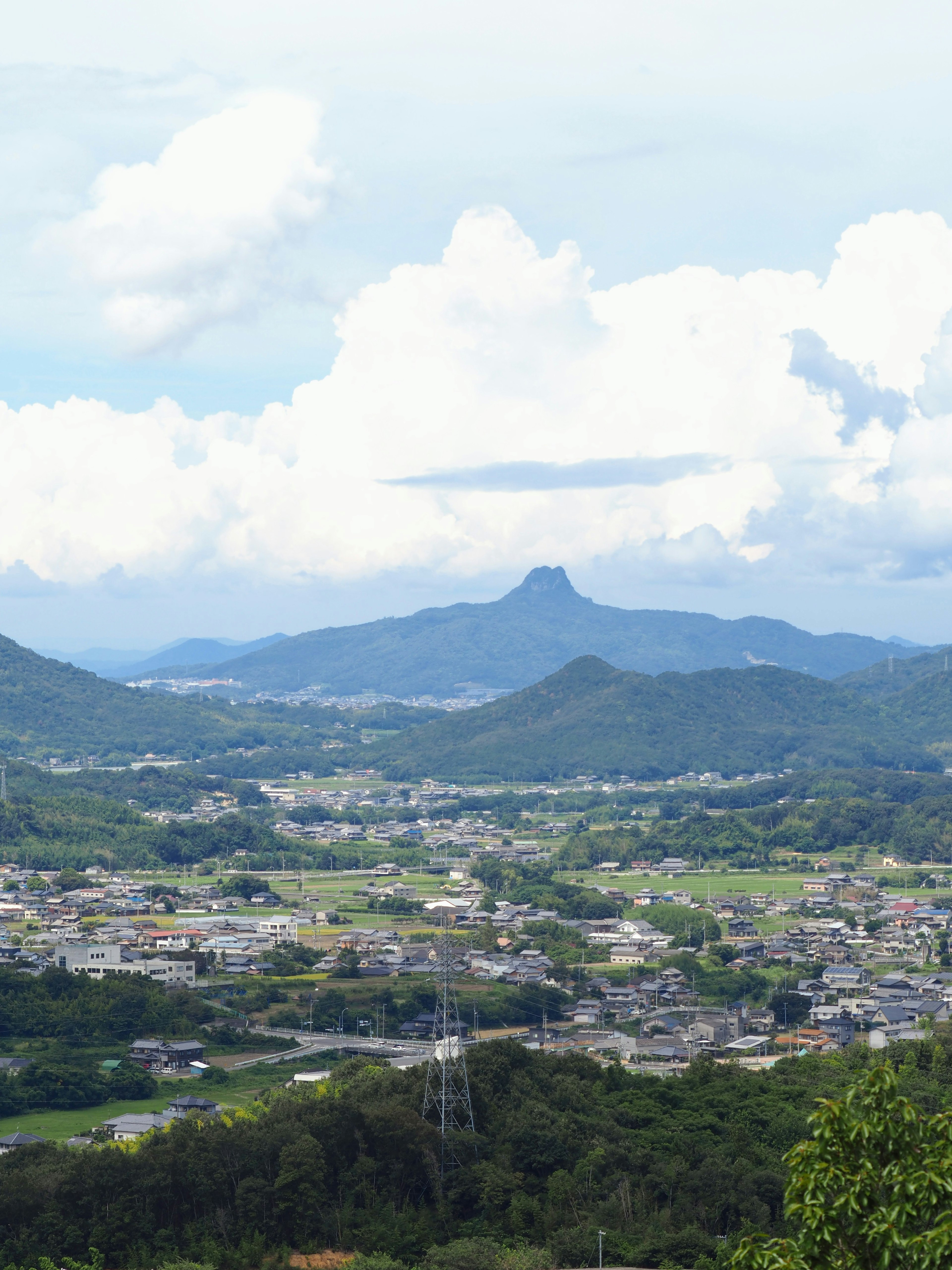 青い空と白い雲が広がる風景に、山と村が見える