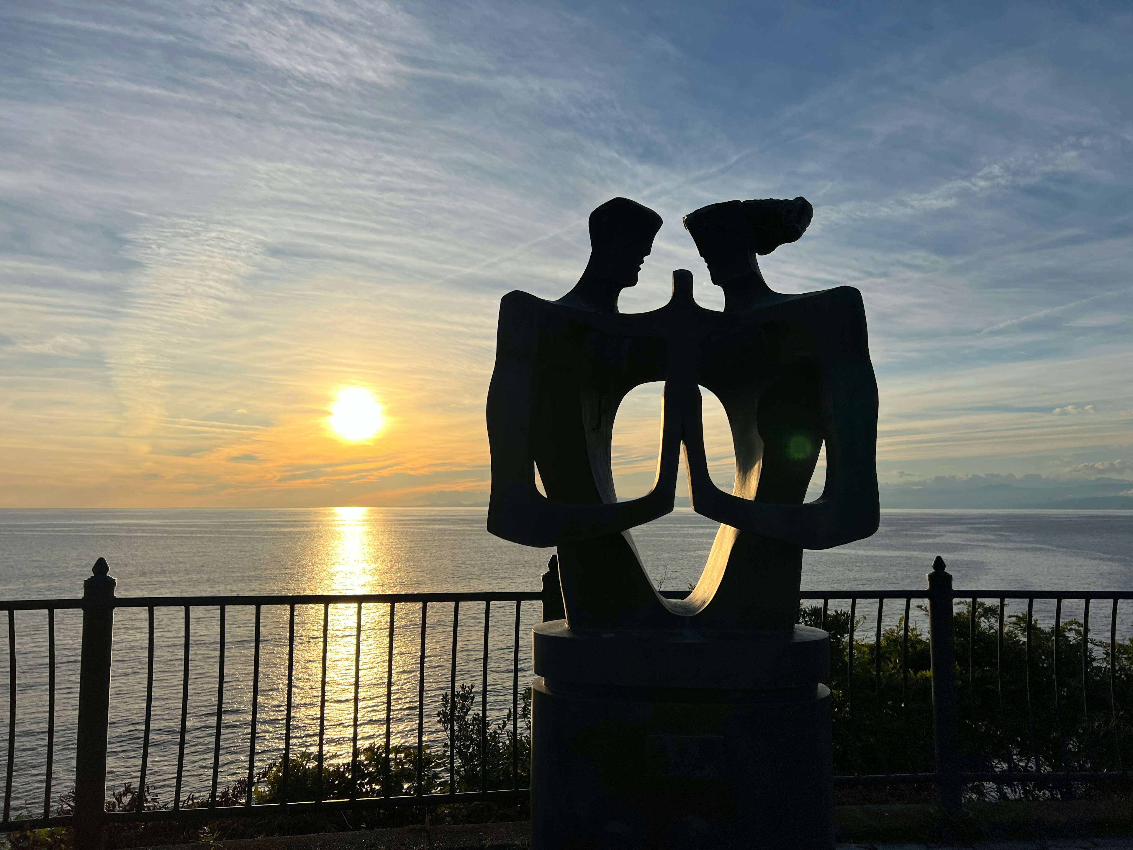 Abstract sculpture of two figures facing each other with the sunset over the ocean