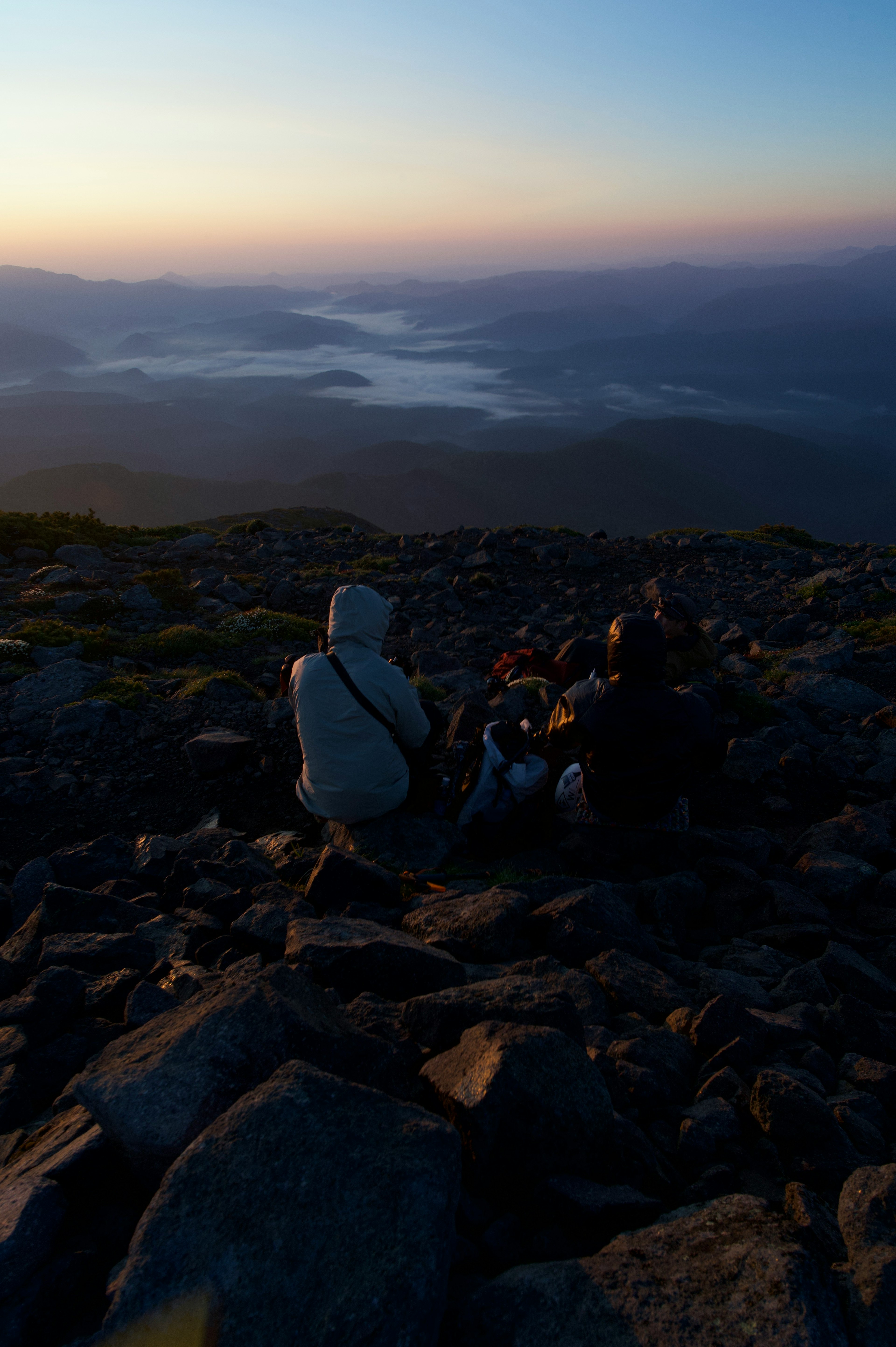 Zwei Personen genießen die Aussicht von einem Berggipfel mit einem See im Hintergrund