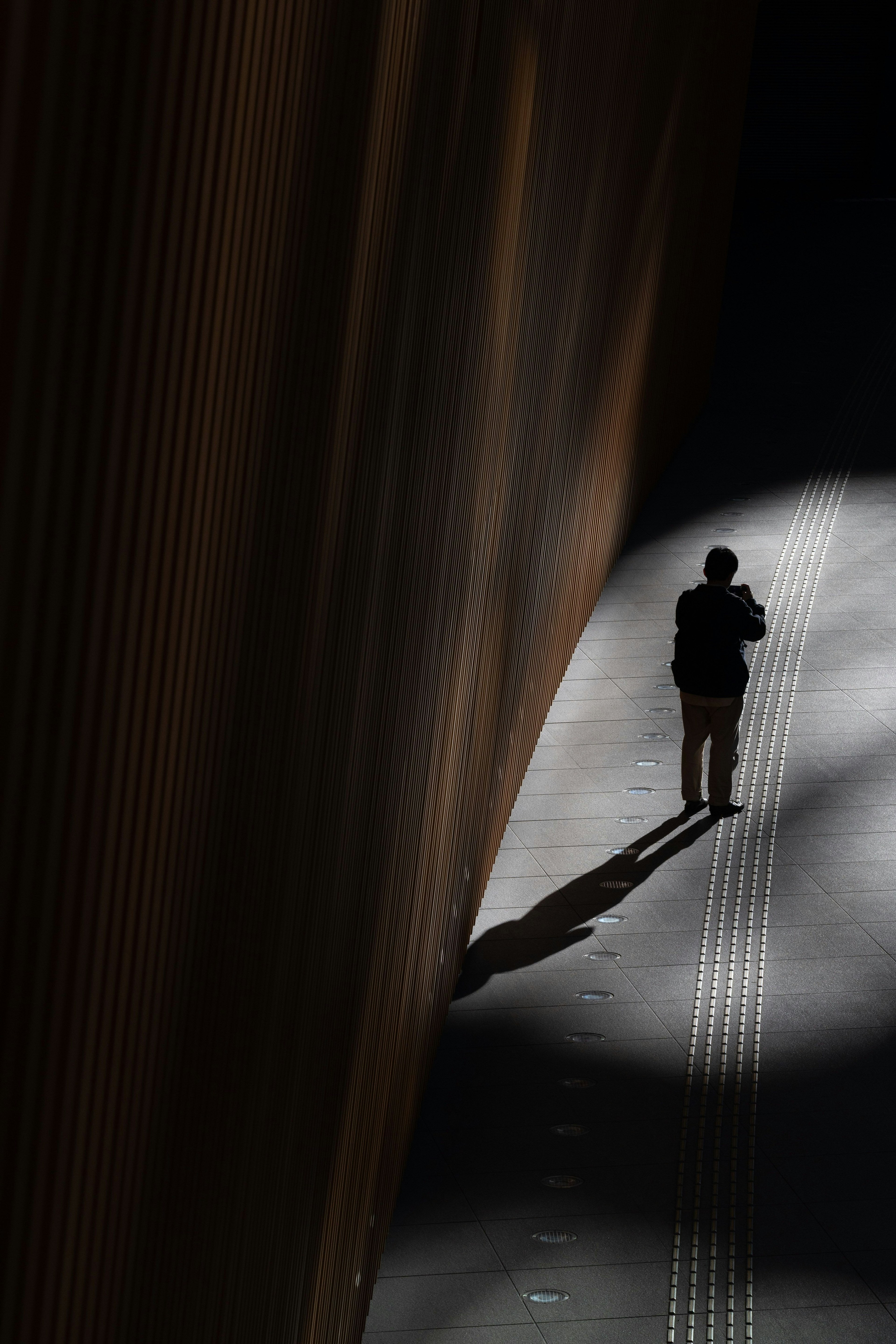 Una persona de pie en la sombra con un fuerte contraste de luz en un entorno urbano