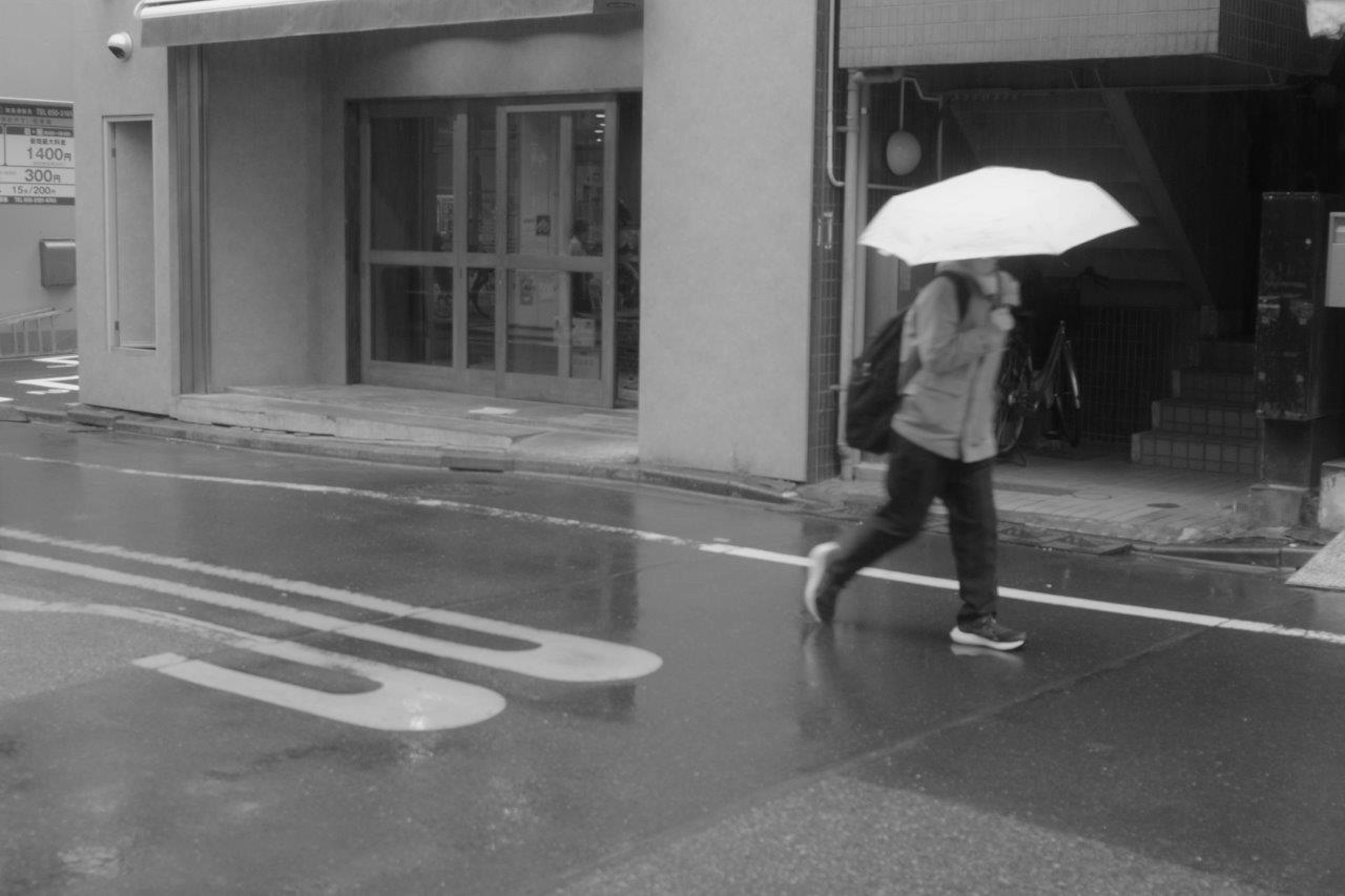 白い傘を持って歩く人が映る雨の街並み