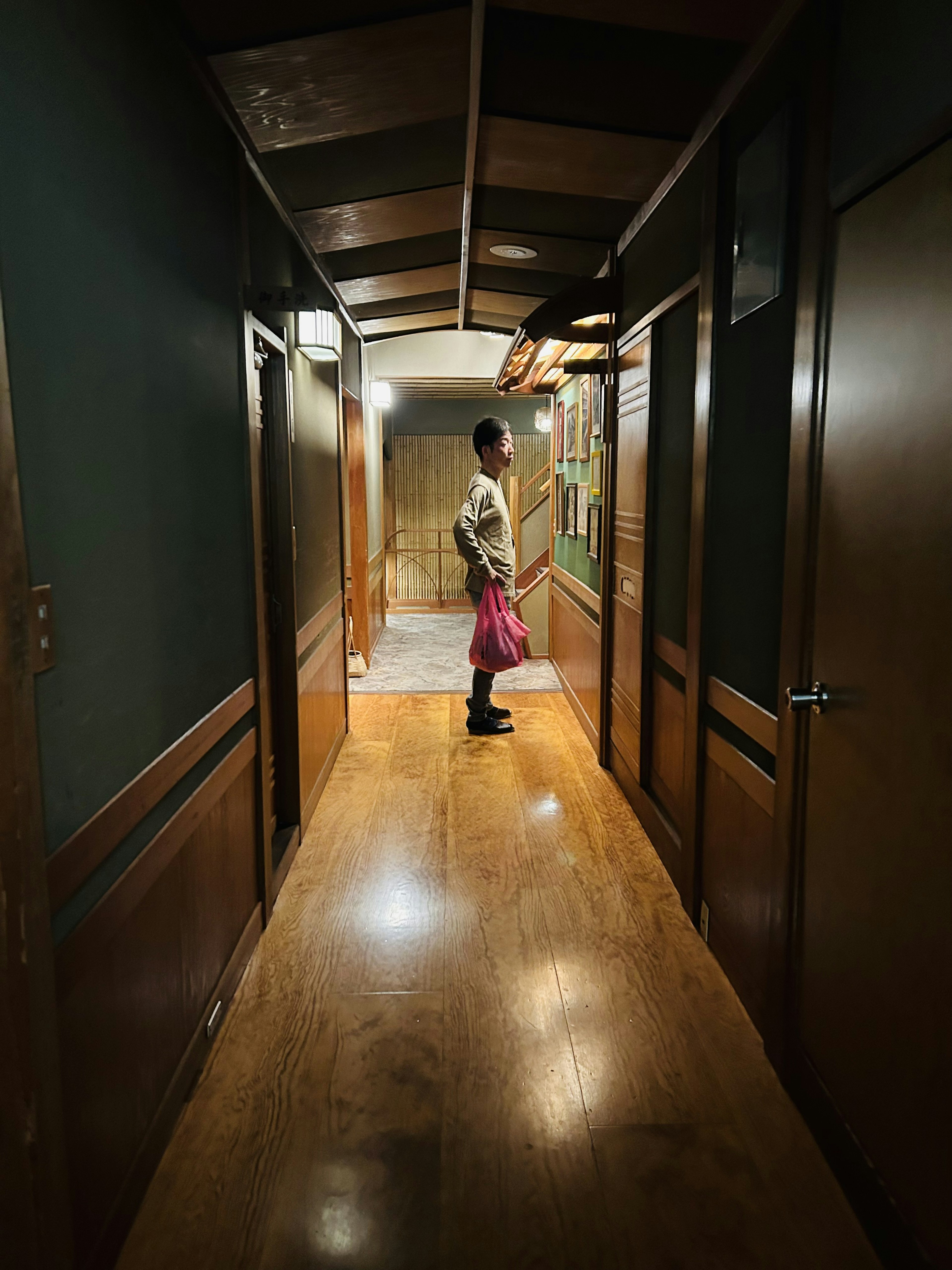 Person standing in a long hallway with wooden floors and walls