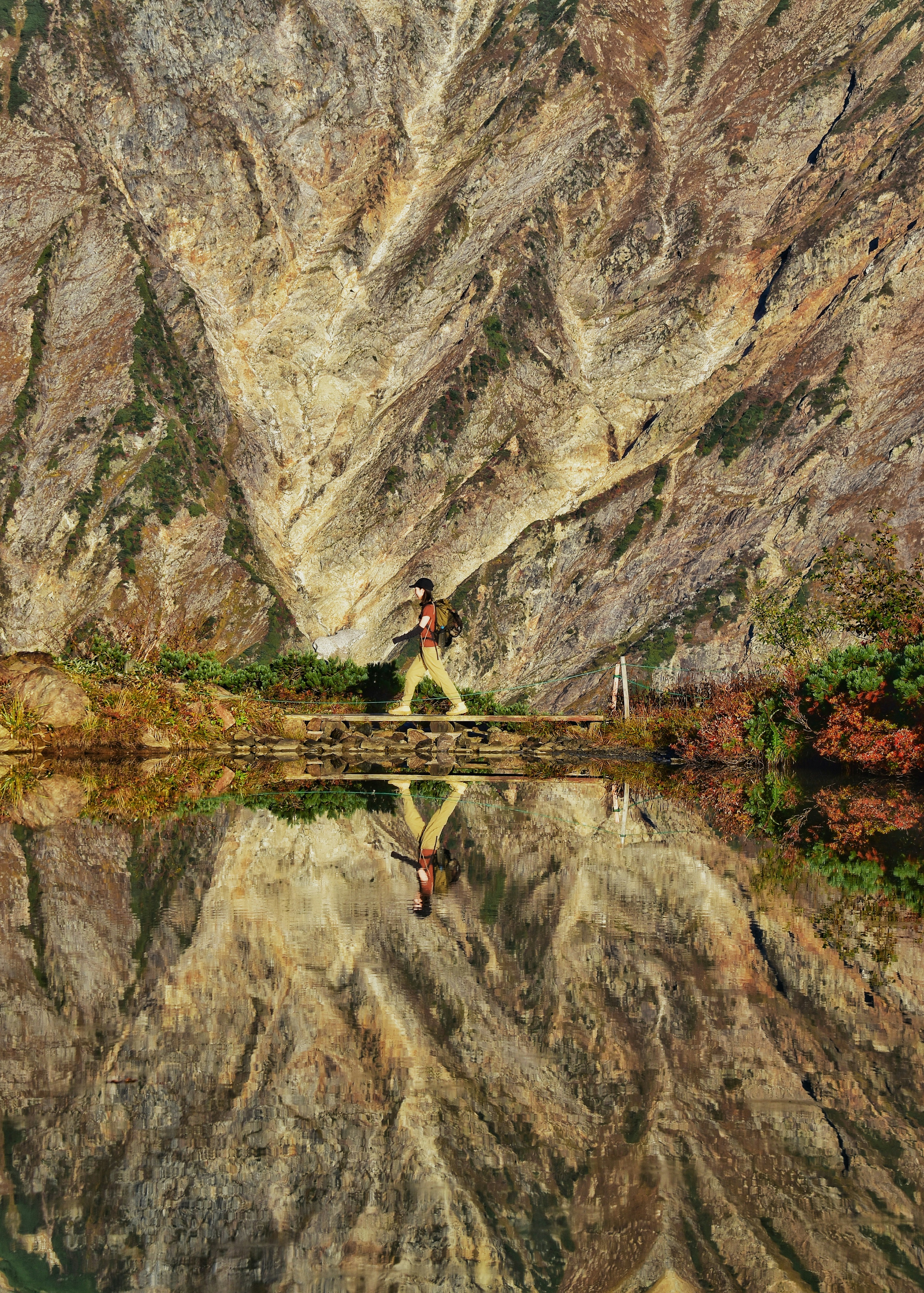 Person walking near a lake reflecting stunning mountain scenery