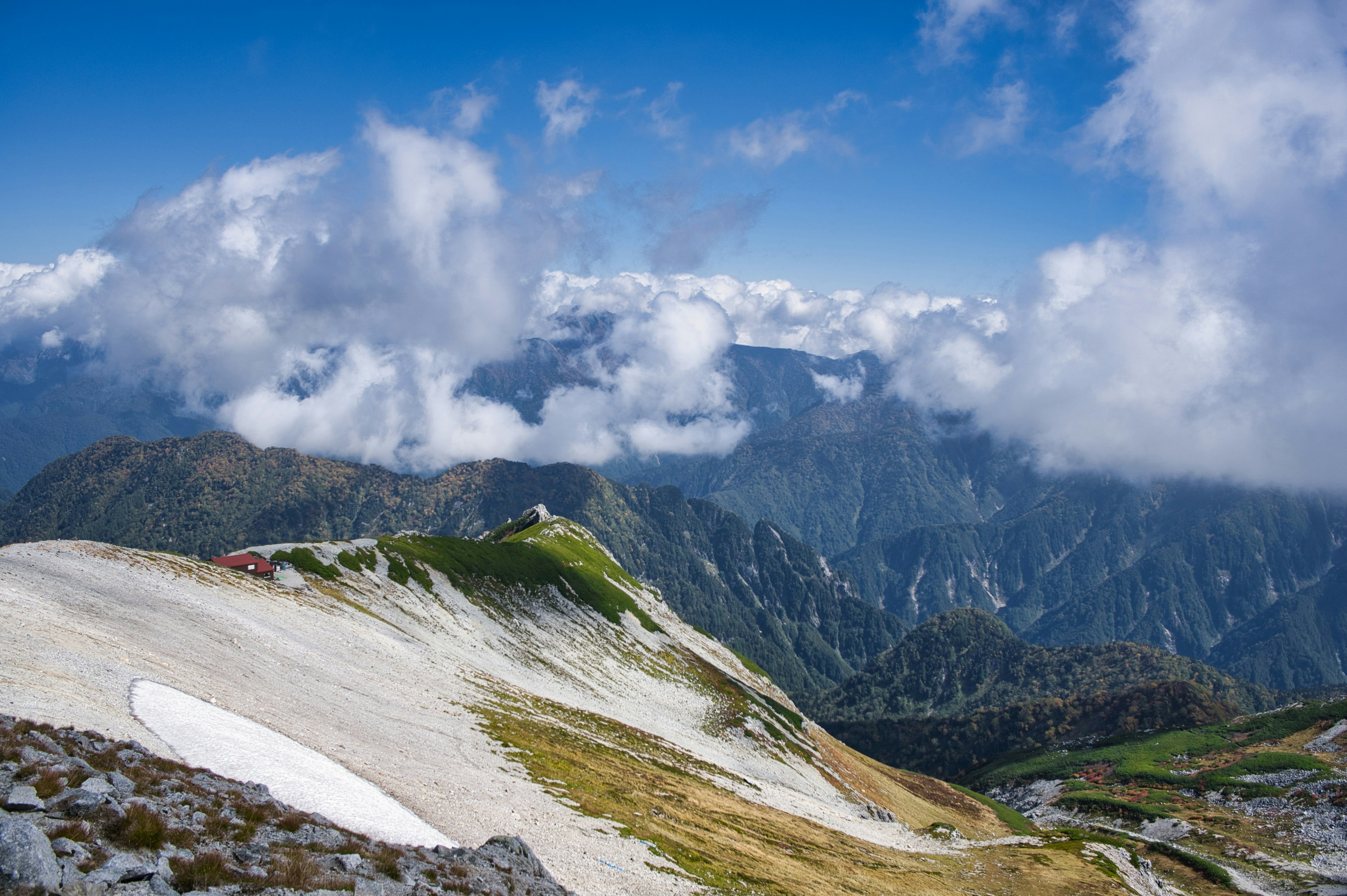 美丽的山景被蓝天和白云环绕，绿色草地和山坡上的残雪