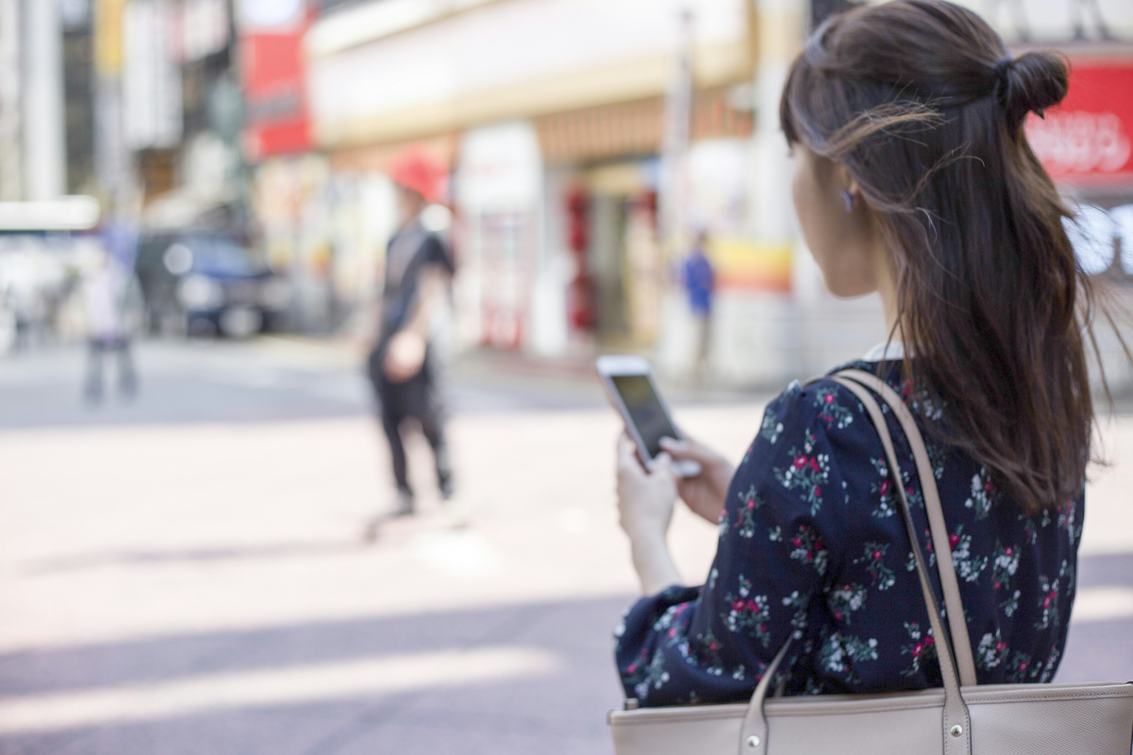 Mujer usando un smartphone en la esquina de la calle con personas y tiendas de fondo