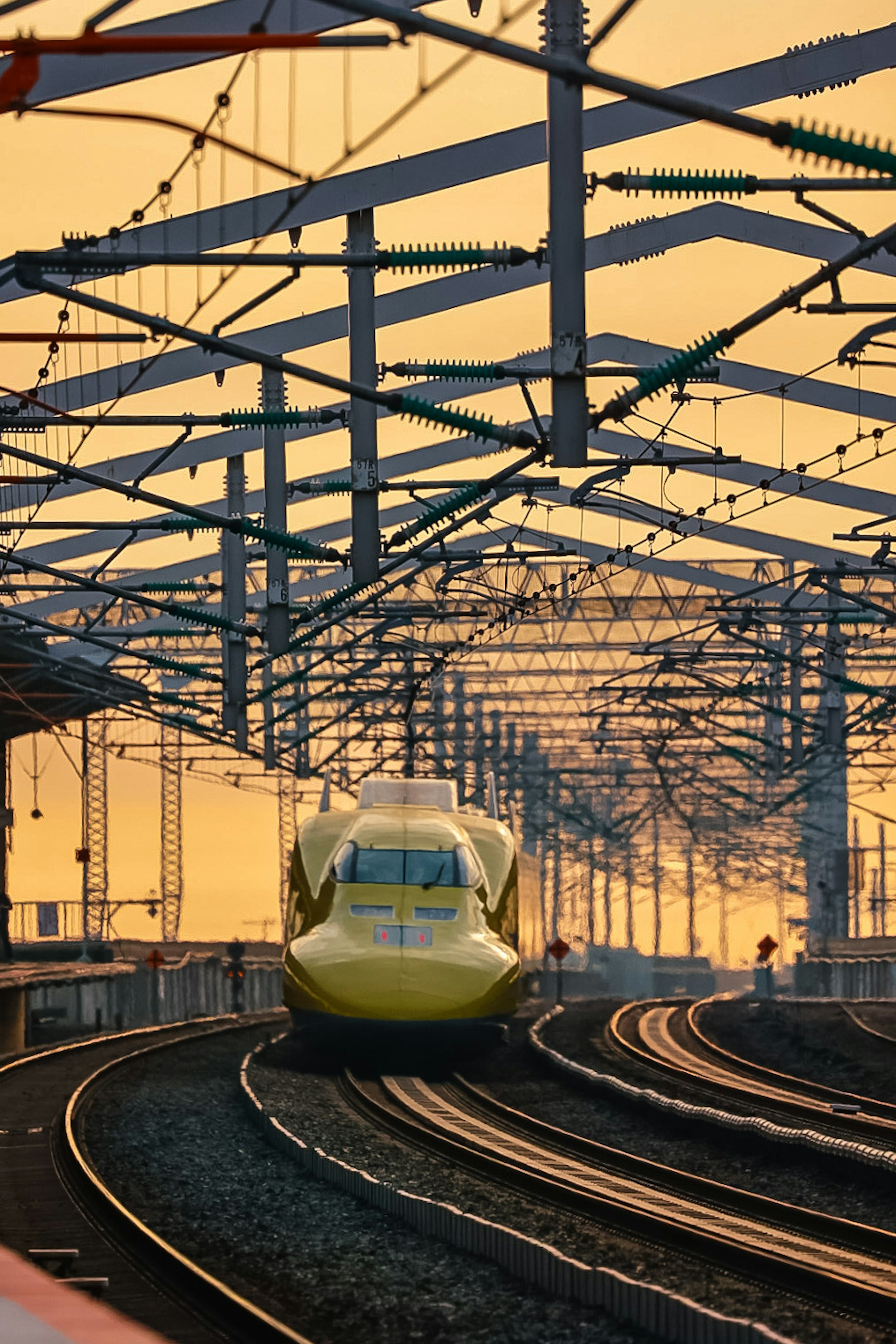 Yellow Shinkansen train on curved tracks under a sunset sky