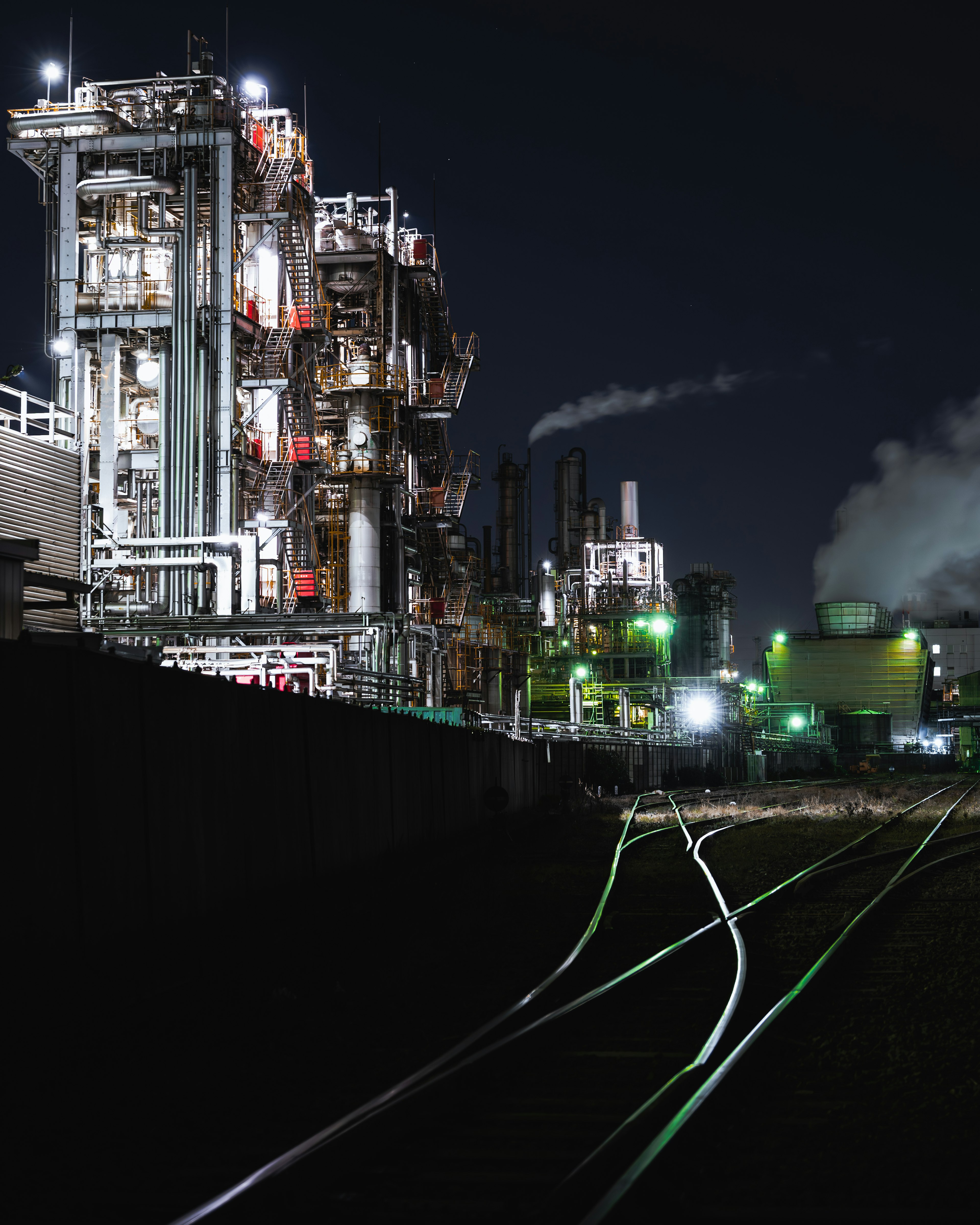 Nighttime industrial scene with illuminated factory structures and smoke emitting chimneys