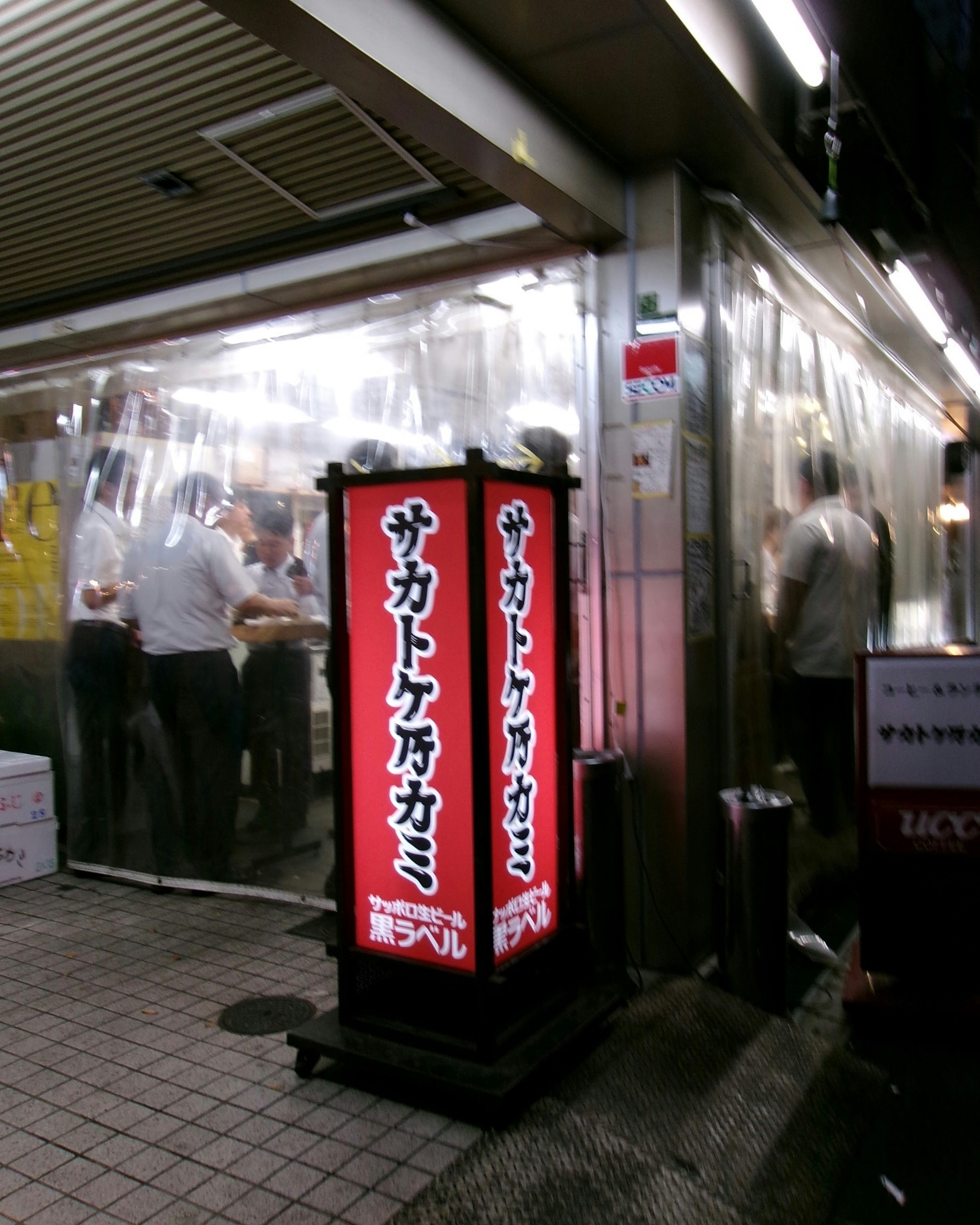 Exterior de un restaurante japonés Cartel rojo brillante y cortinas de vinilo transparentes Personas cenando en el interior