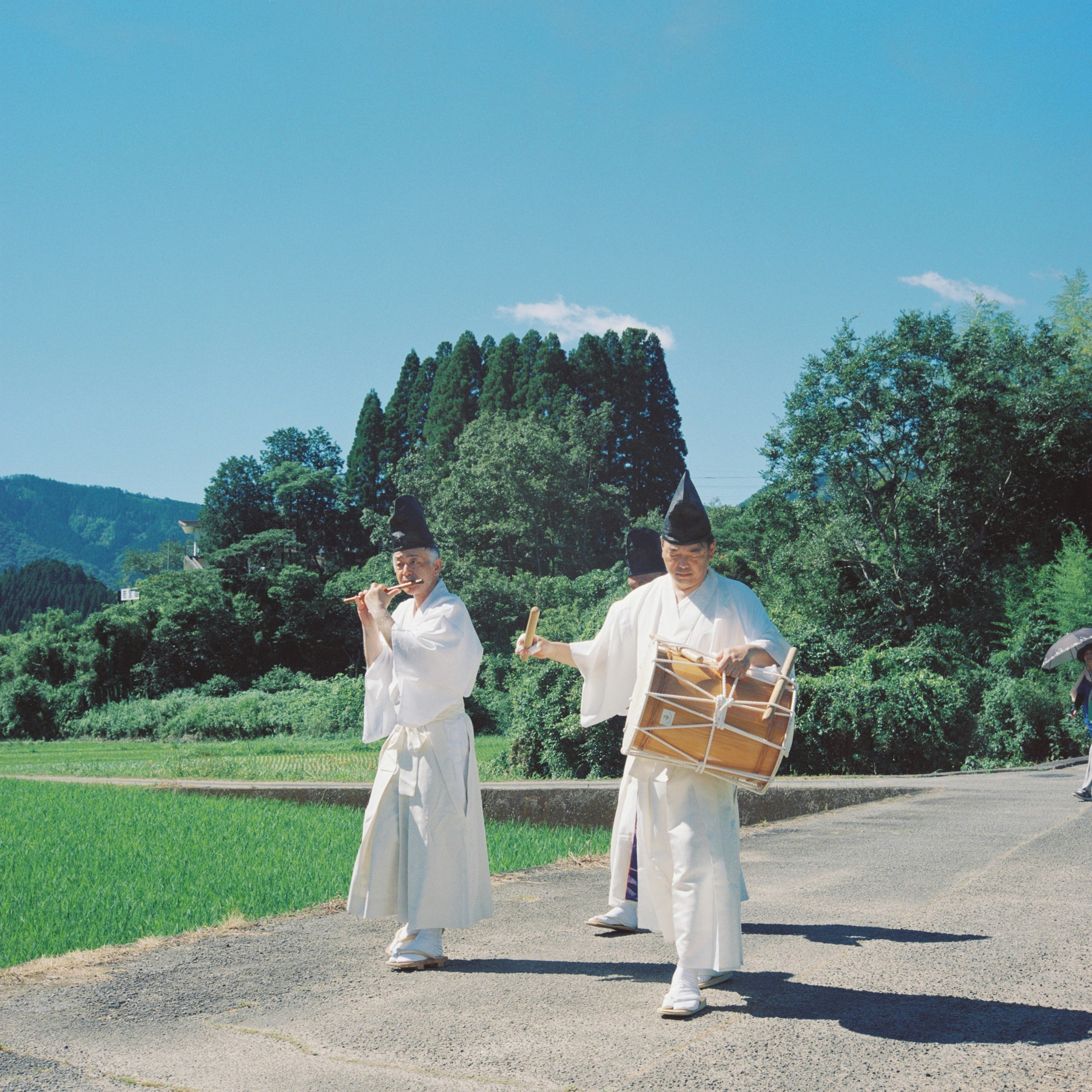 Two traditional musicians in white attire walking along a rural path