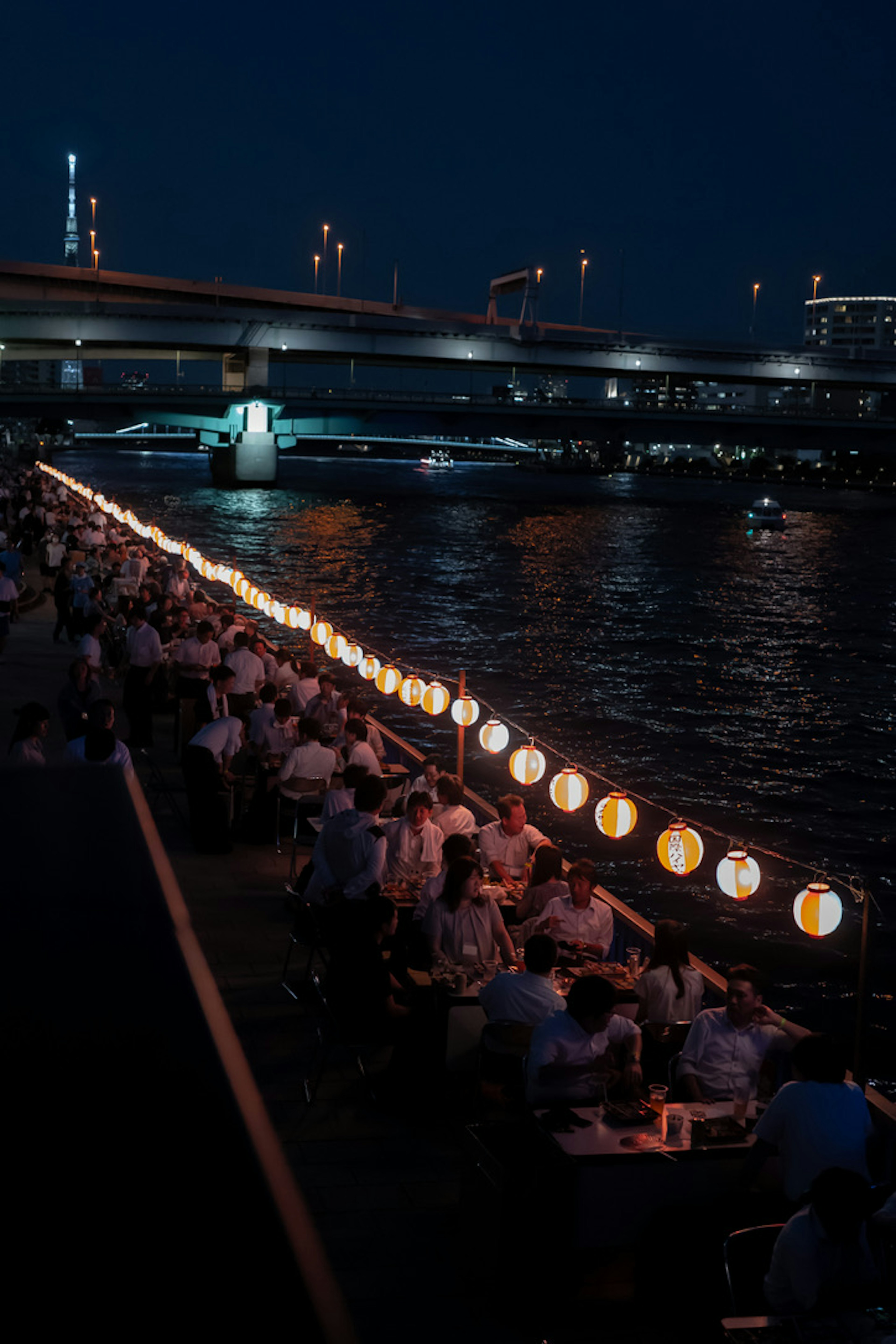 Persone che cenano sotto lanterne lungo il fiume di notte