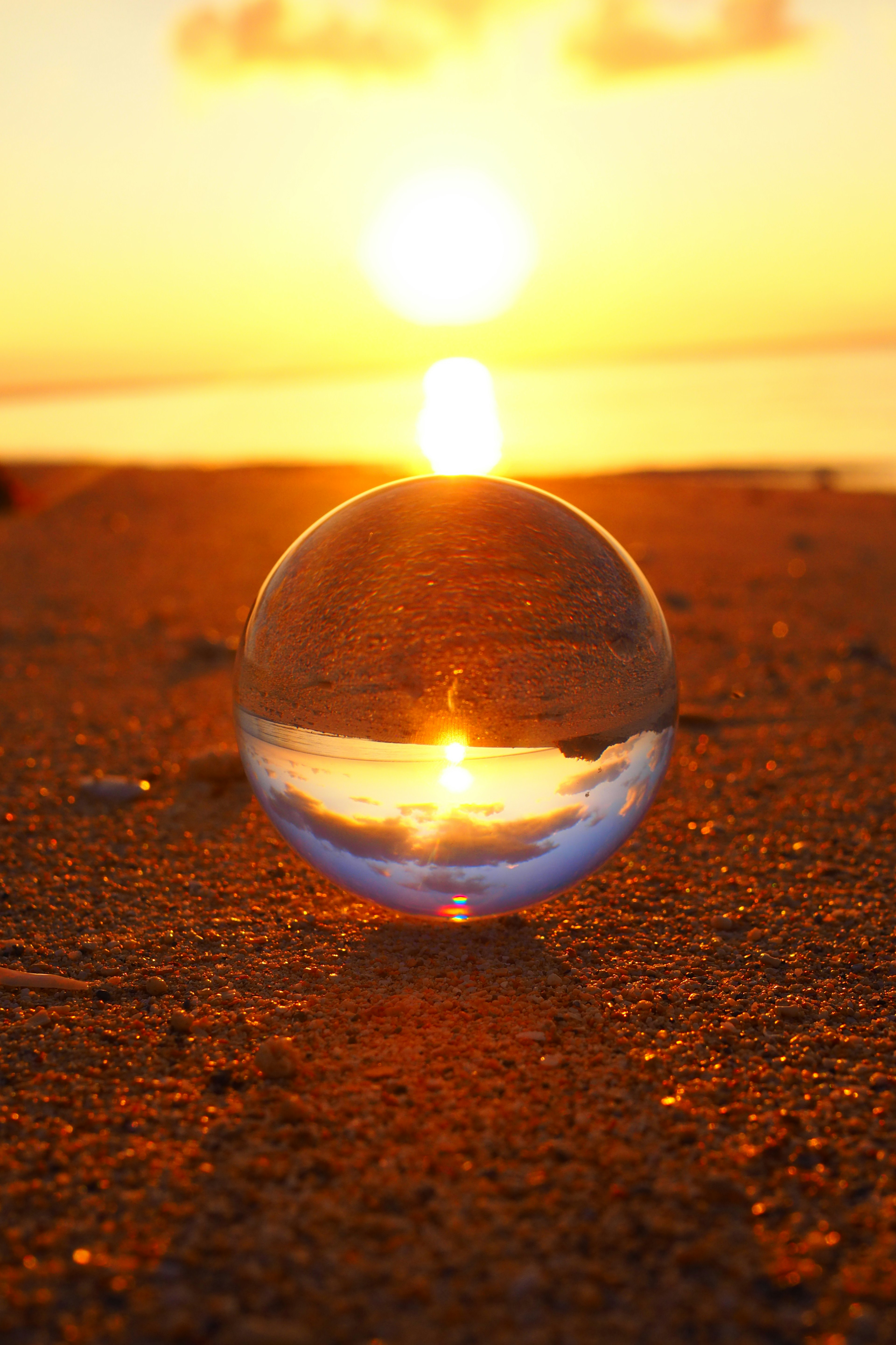 Kristallkugel, die den Sonnenuntergang an einem Sandstrand reflektiert