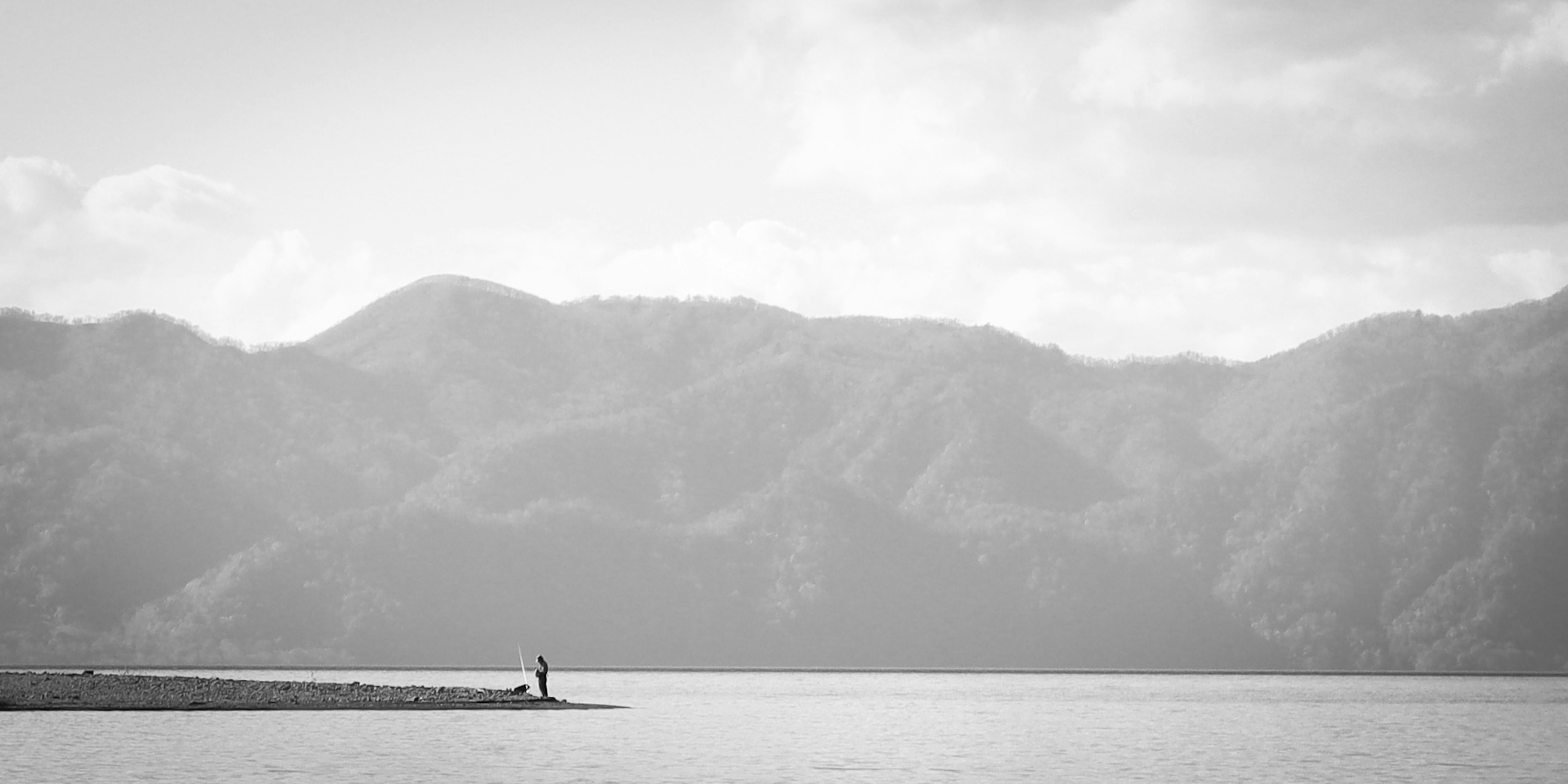 Silhouette einer Person, die an einem ruhigen See steht, mit Bergen im Hintergrund