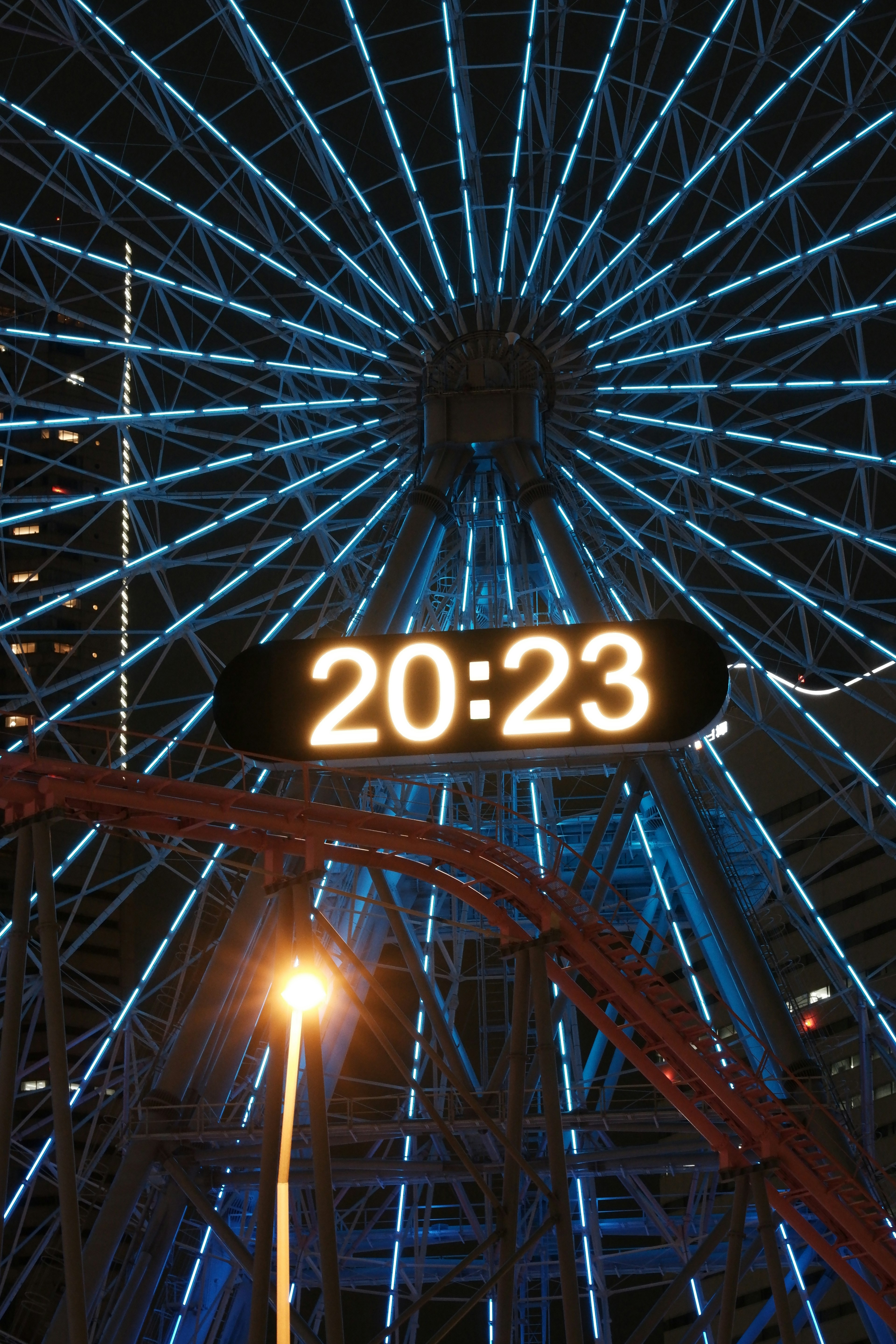 Rueda de la fortuna iluminada por la noche con luces azules y reloj digital