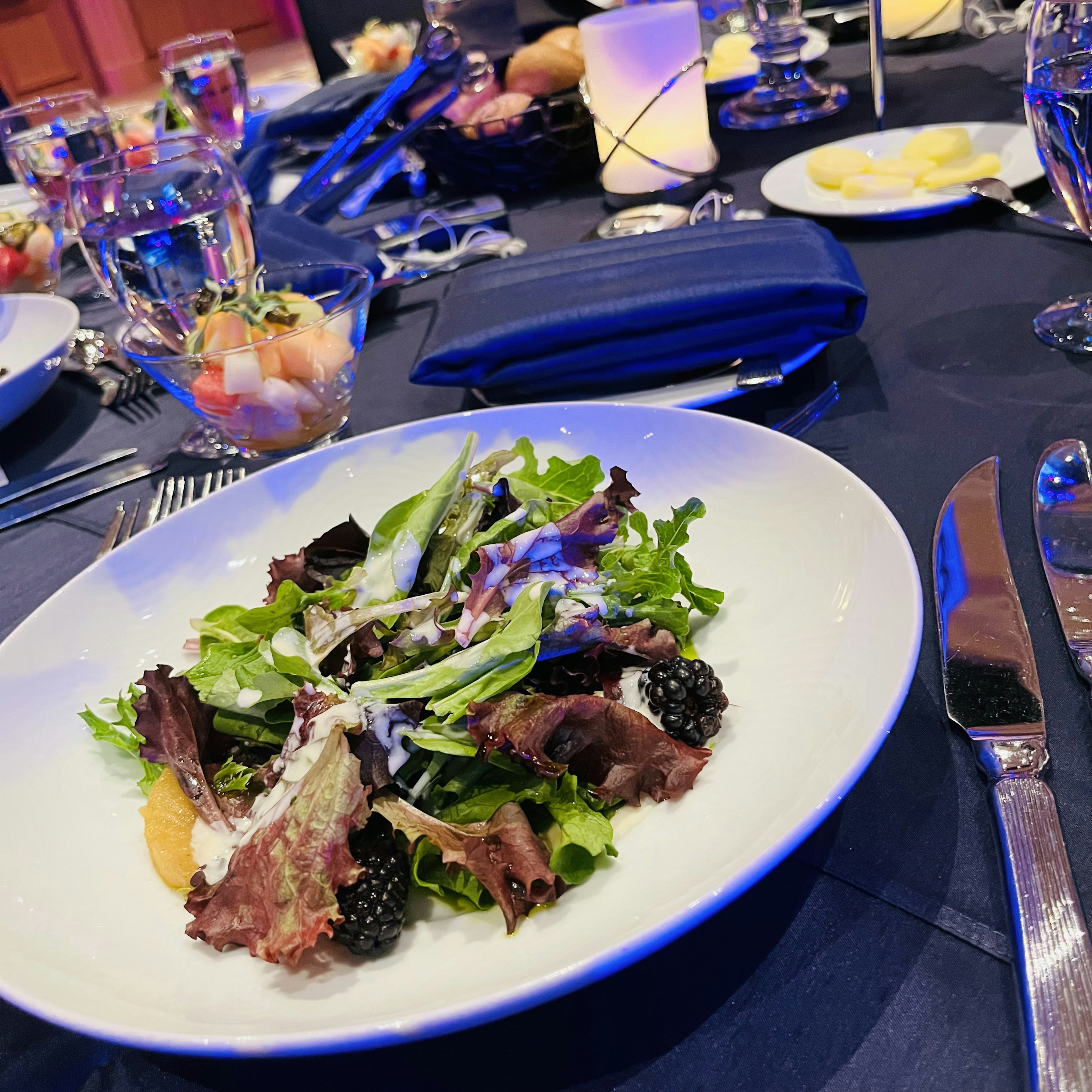 A salad plate on a dining table featuring fresh leafy greens and blackberries