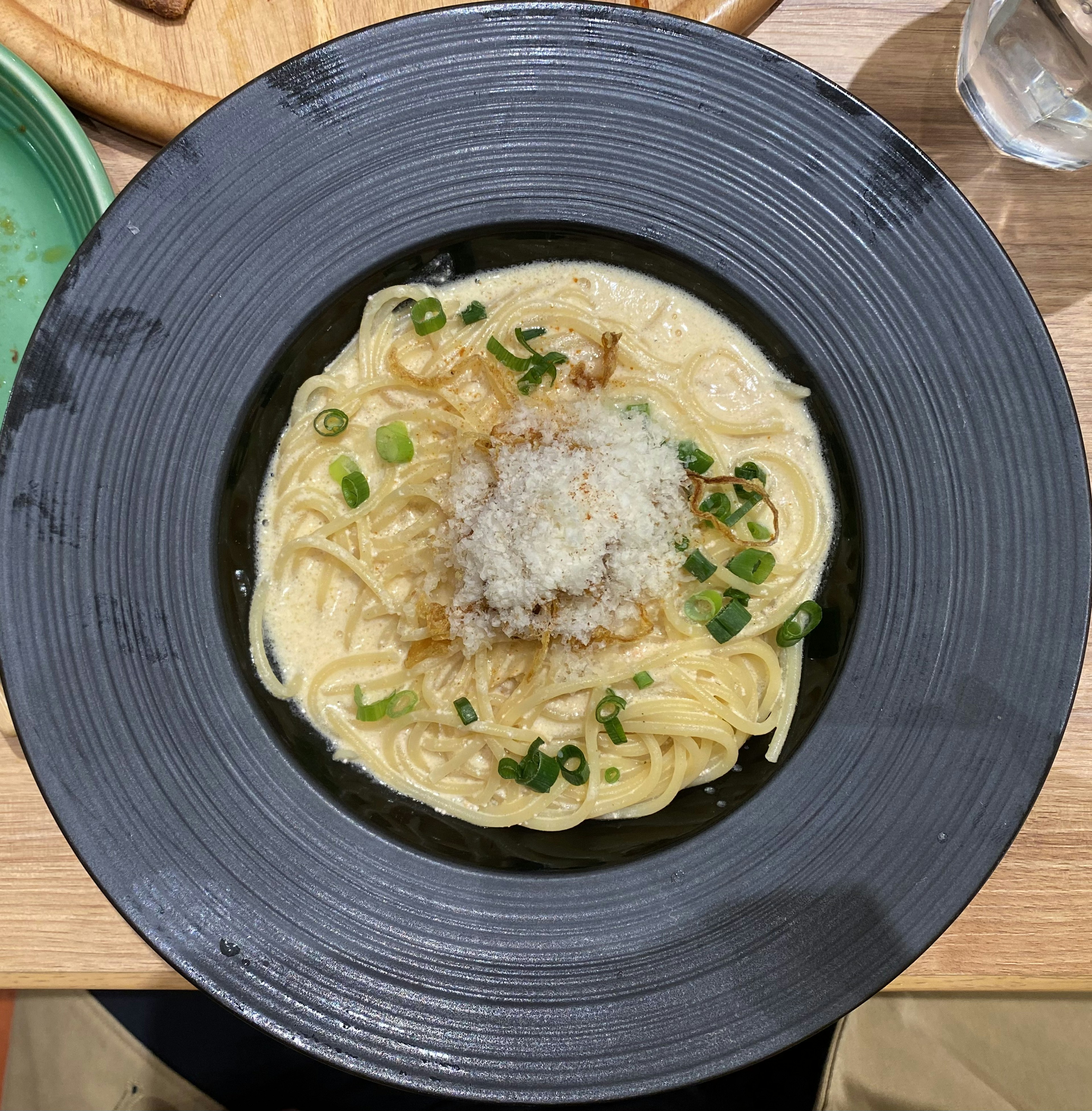 Udon cremoso servido en un tazón negro cubierto con cebollitas verdes y copos de bonito