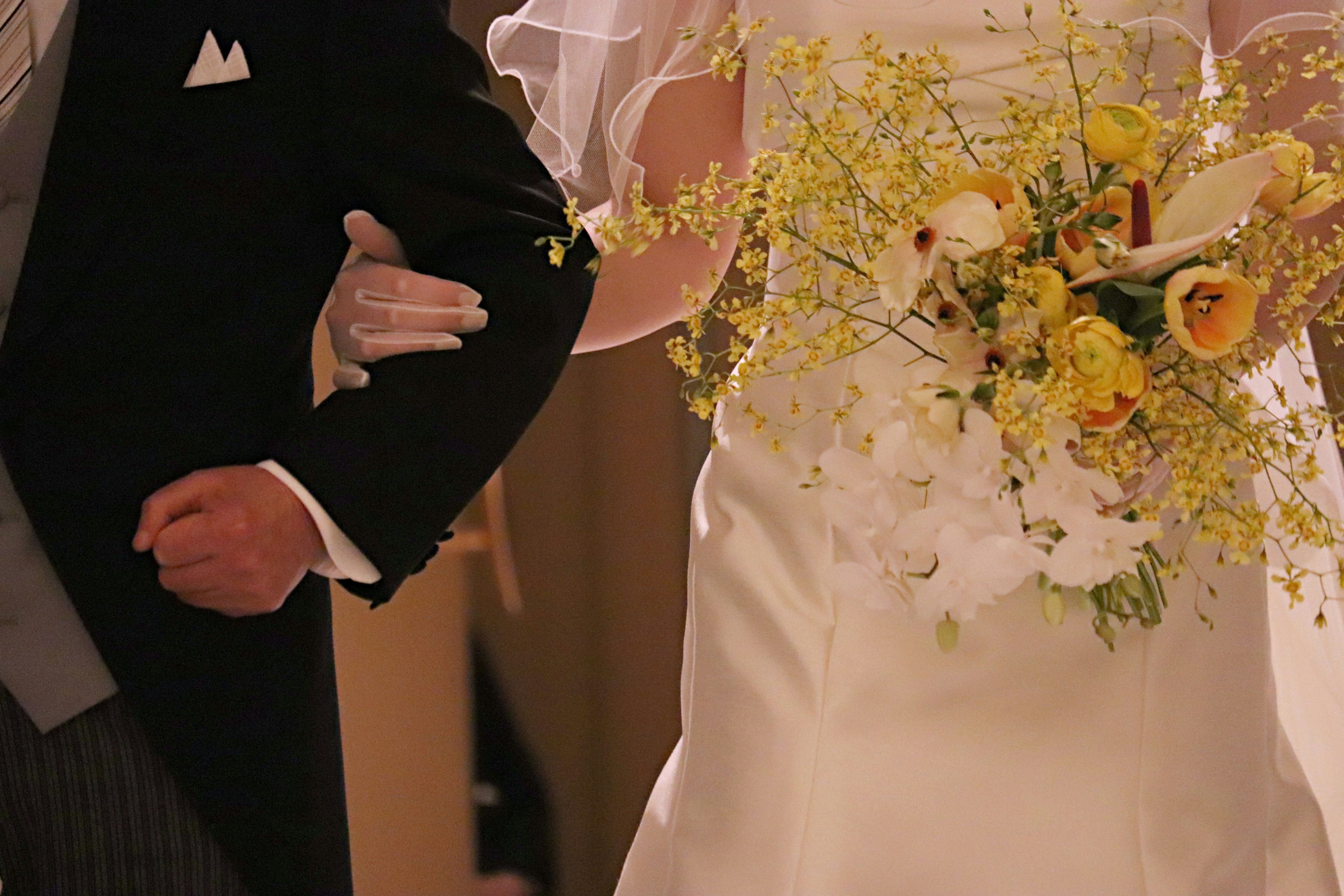 Novia sosteniendo un ramo de boda con el brazo del novio en esmoquin