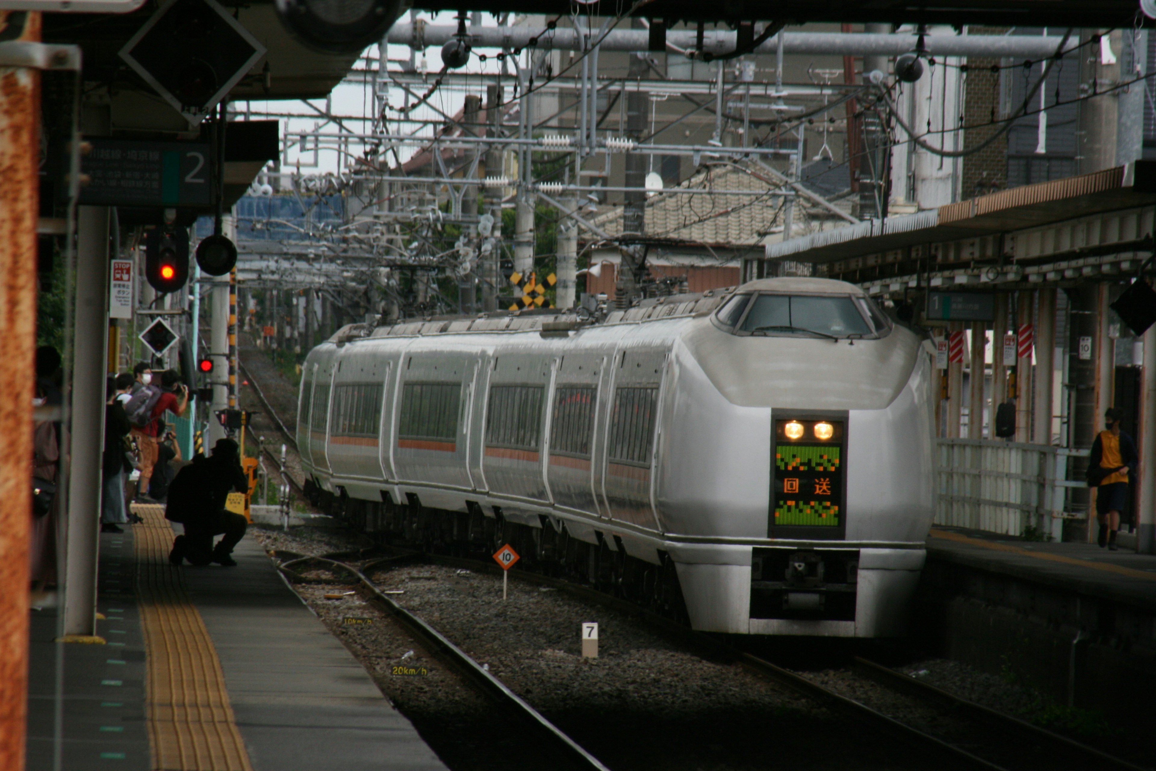 A silver train approaching the station with people visible nearby