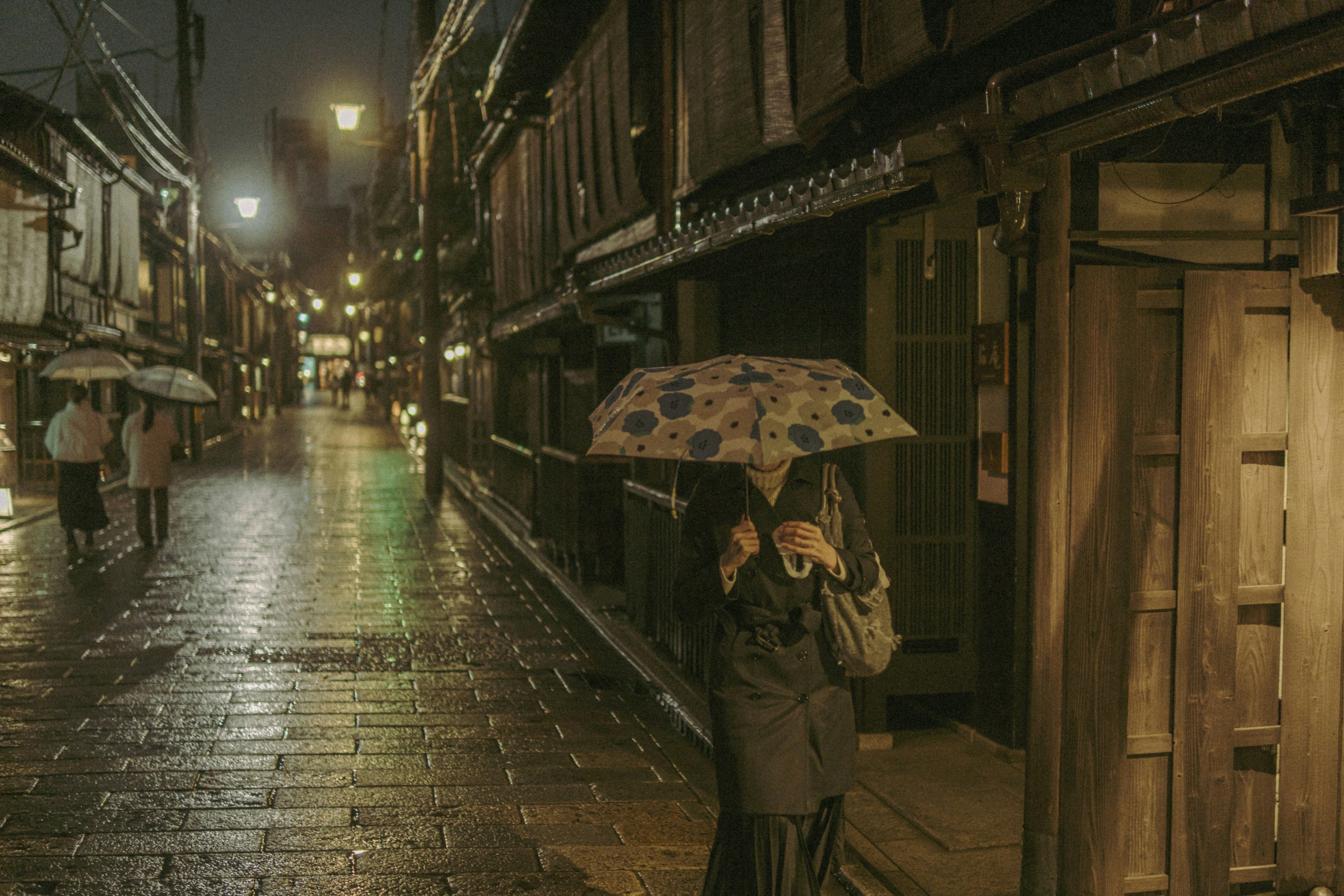 夜の街並みを歩く人々と傘を持つ女性の姿