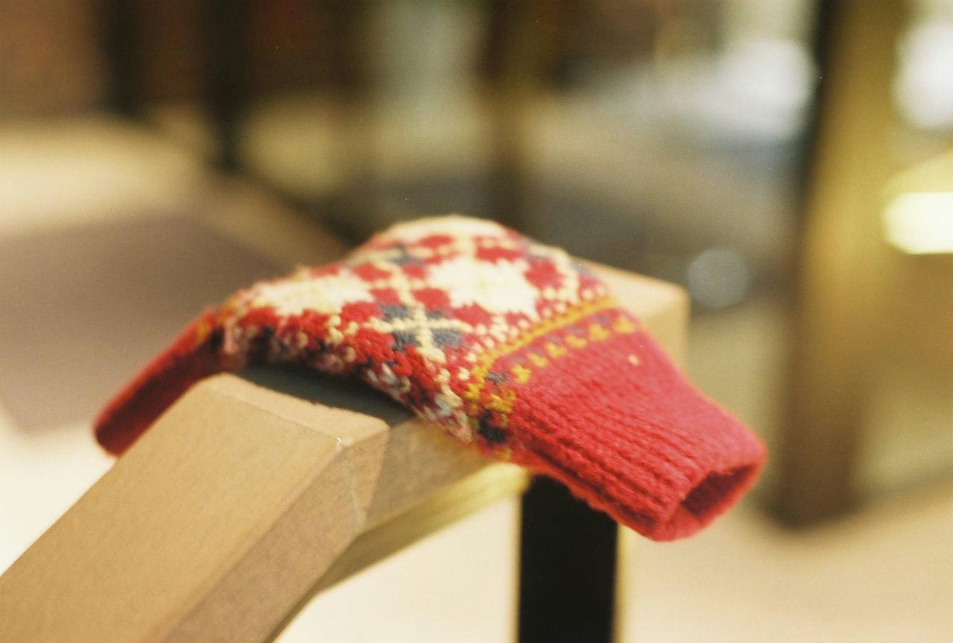 A red knitted mitten resting on a wooden railing