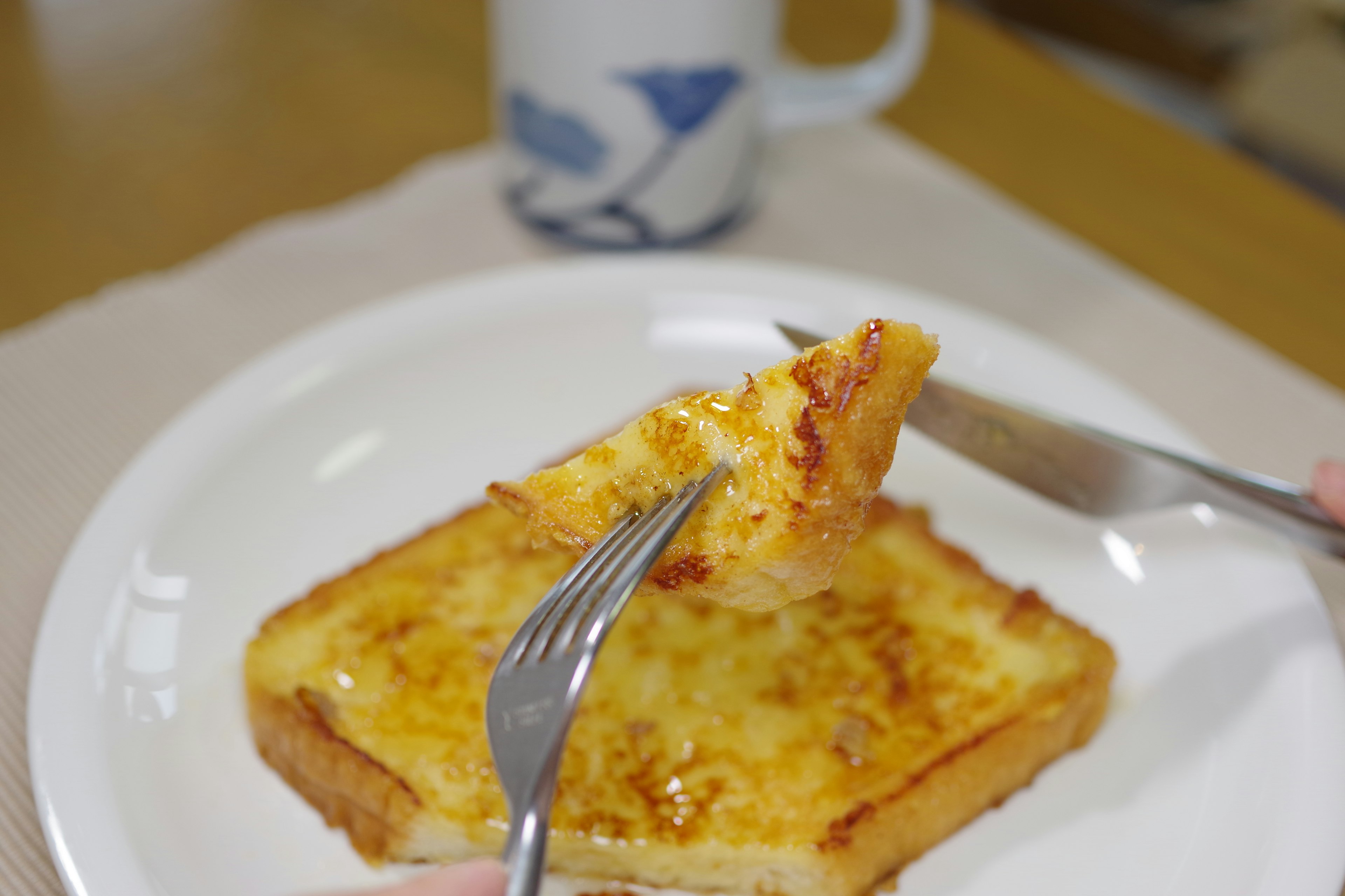 A slice of toasted bread being cut with a fork and knife alongside a cup