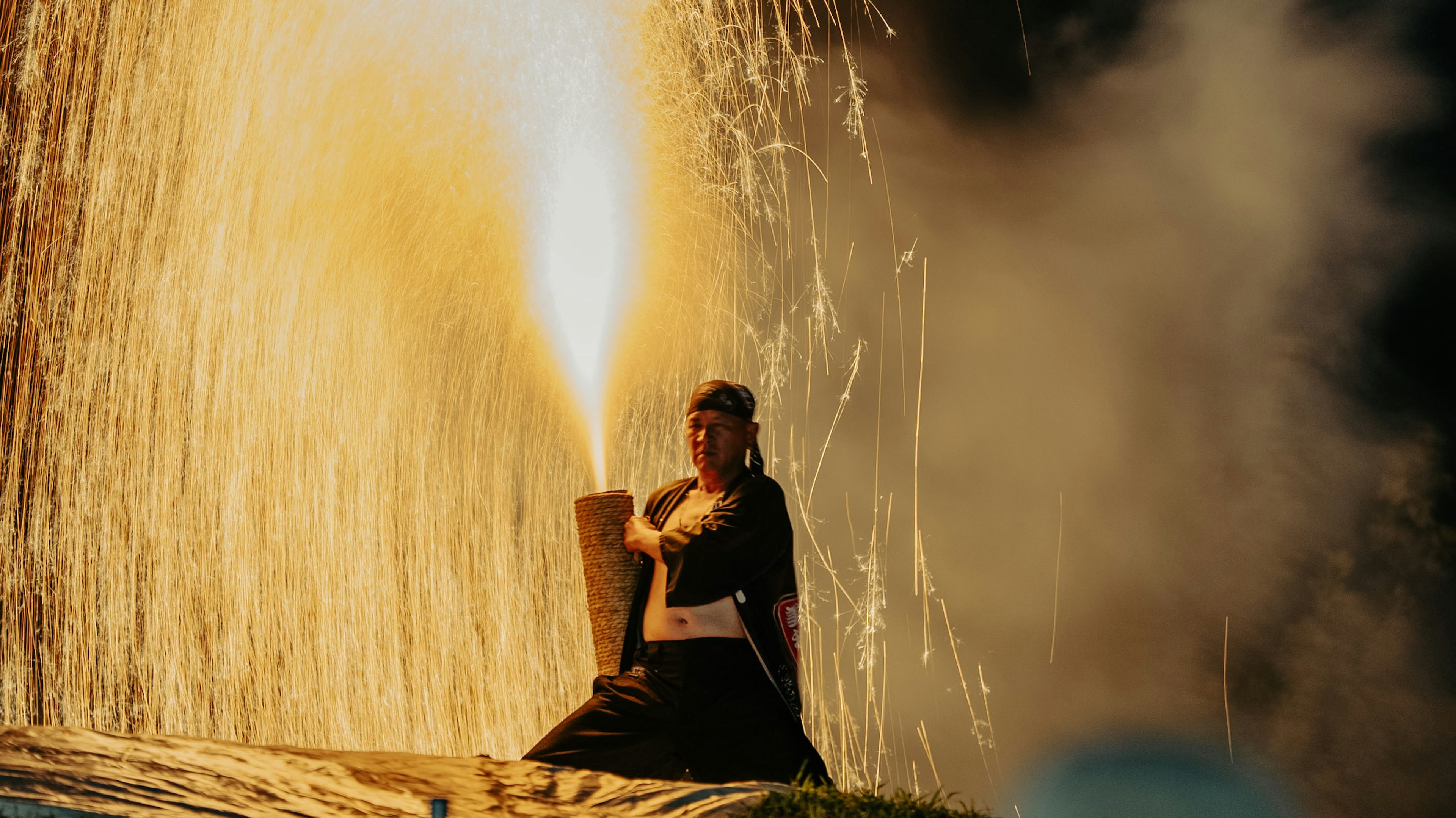 Un artiste assis créant des étincelles avec une torche dans une performance dramatique