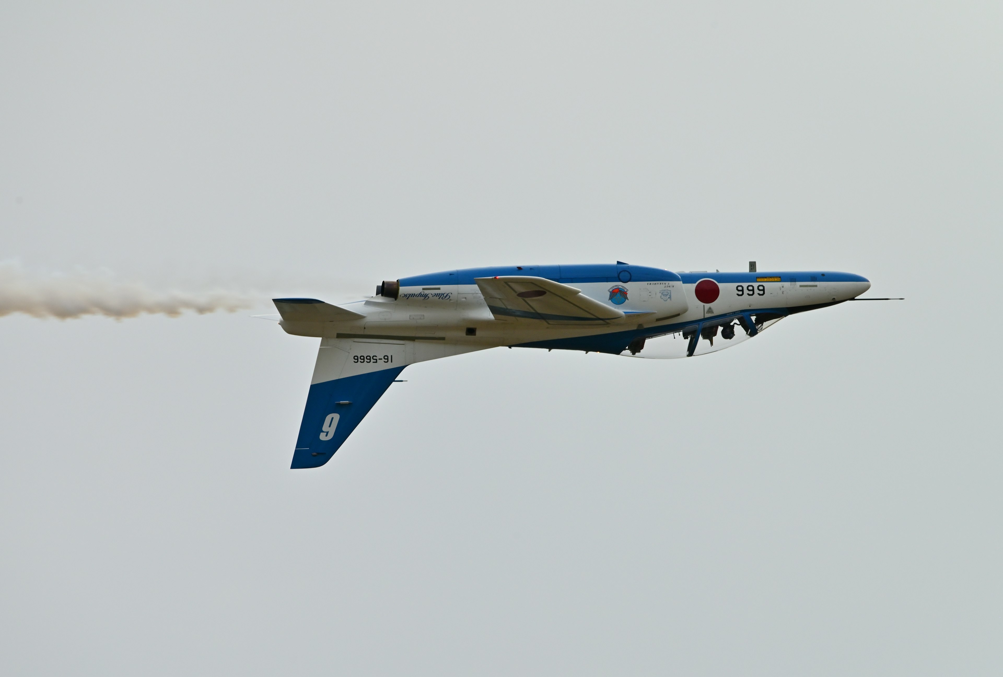 Avión azul y blanco volando con estela de humo