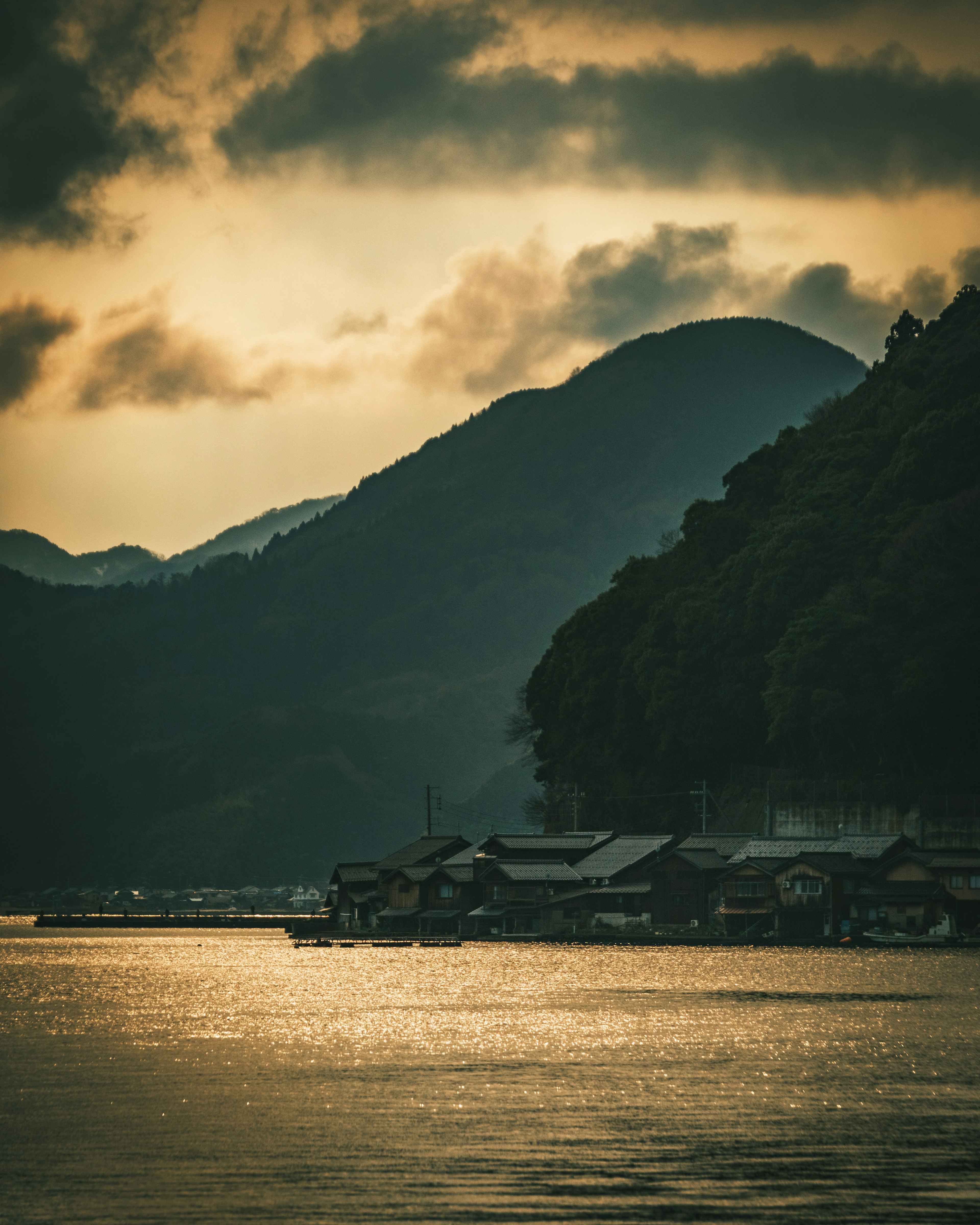 Silhouettierte Häuser am Wasser bei Dämmerung mit Bergen im Hintergrund