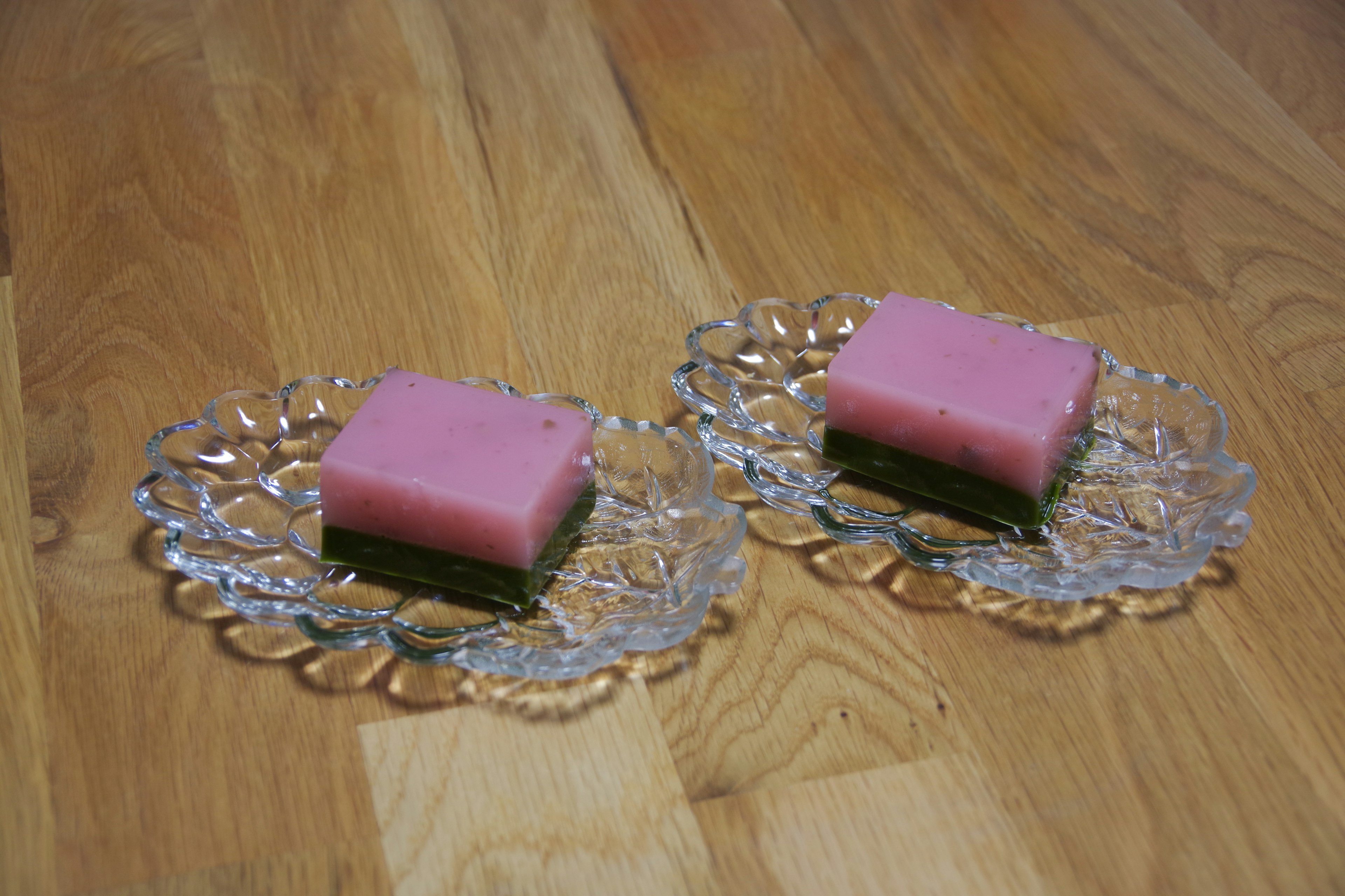 Zwei Kuchen mit rosa und grünen Schichten auf Glasplatten