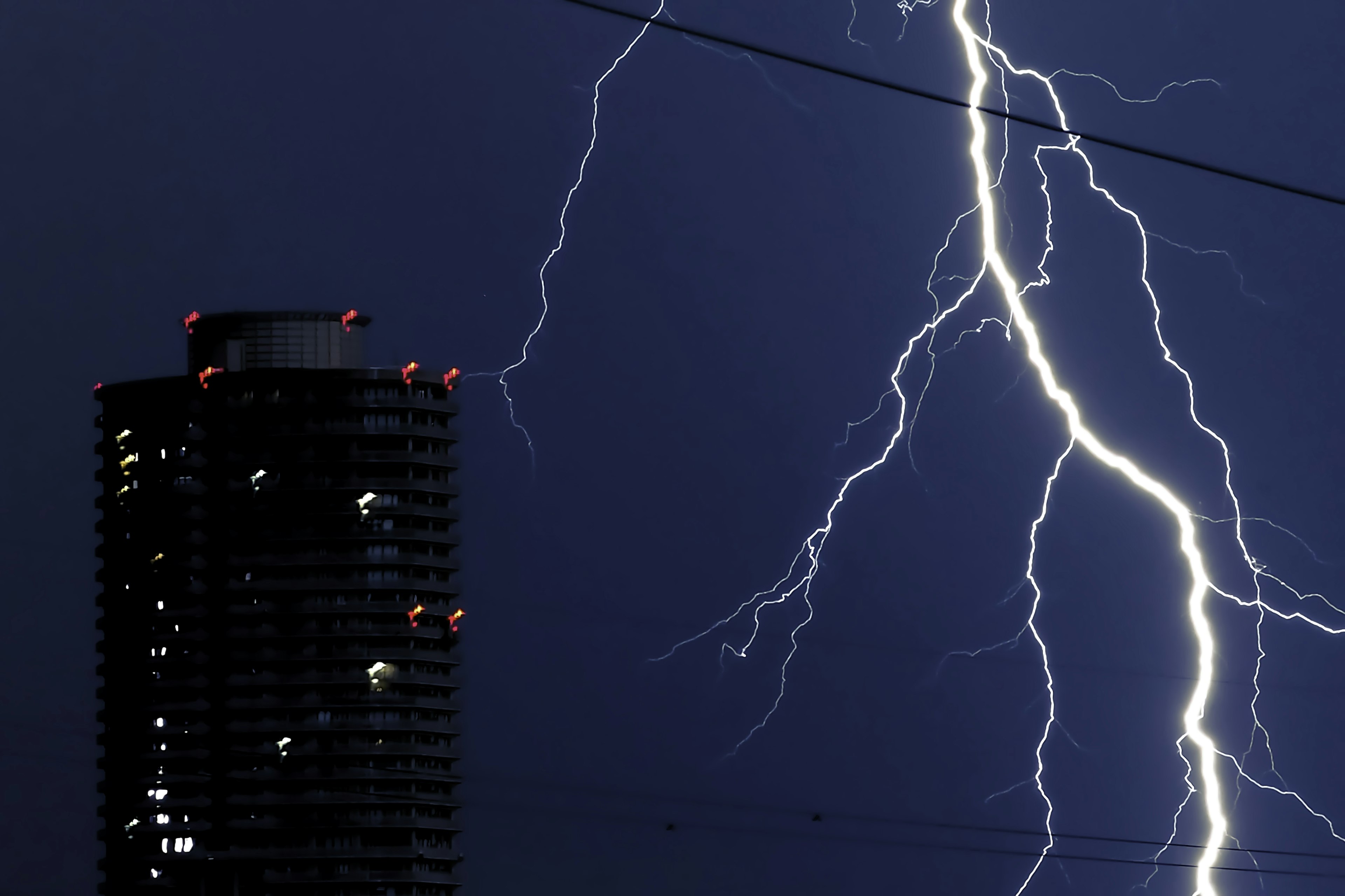 Lightning striking against a dark sky with a tall building