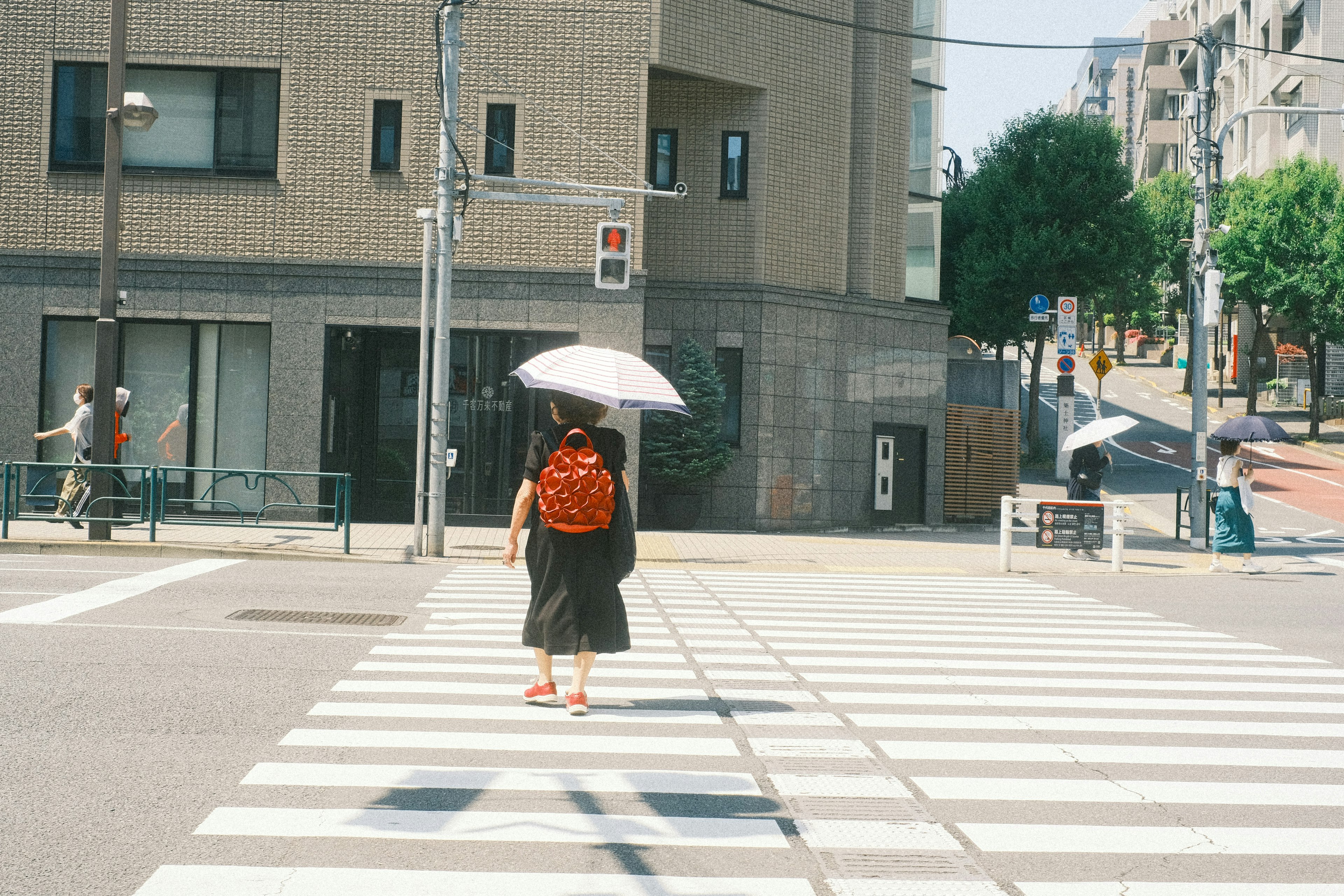 女性が傘を持って横断歩道を渡る街の風景