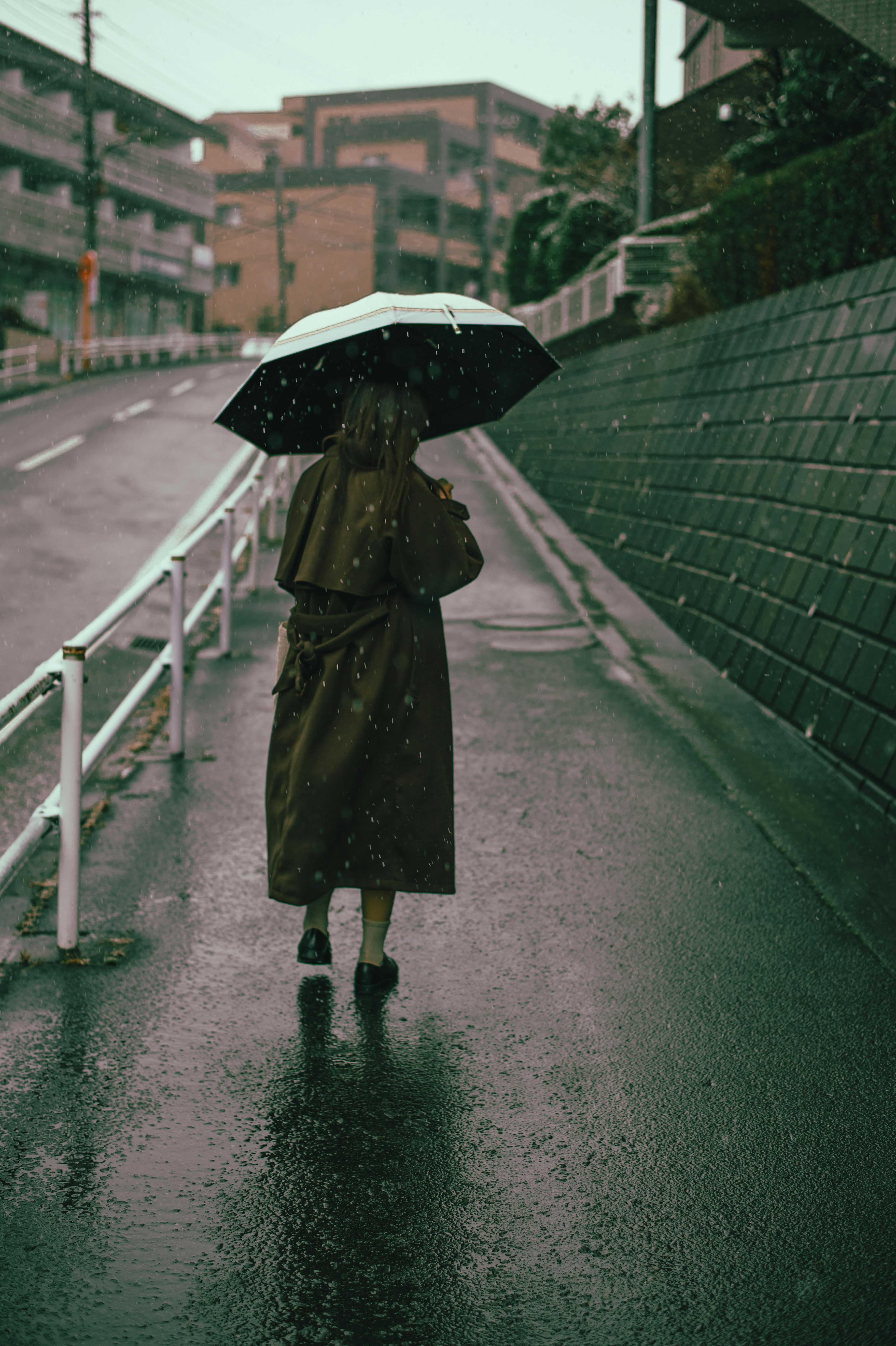 Person walking with an umbrella in the rain, wet road, urban scenery