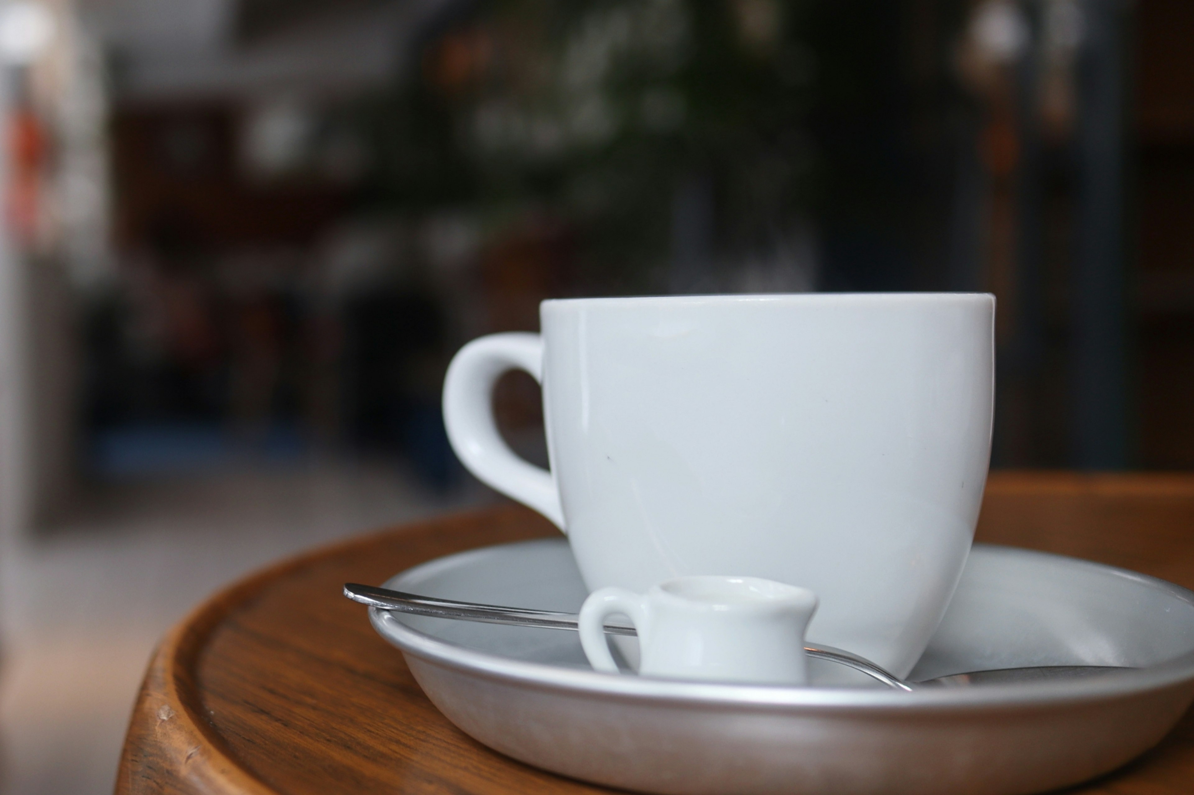 White cup and small milk pitcher on a tray in a cafe setting