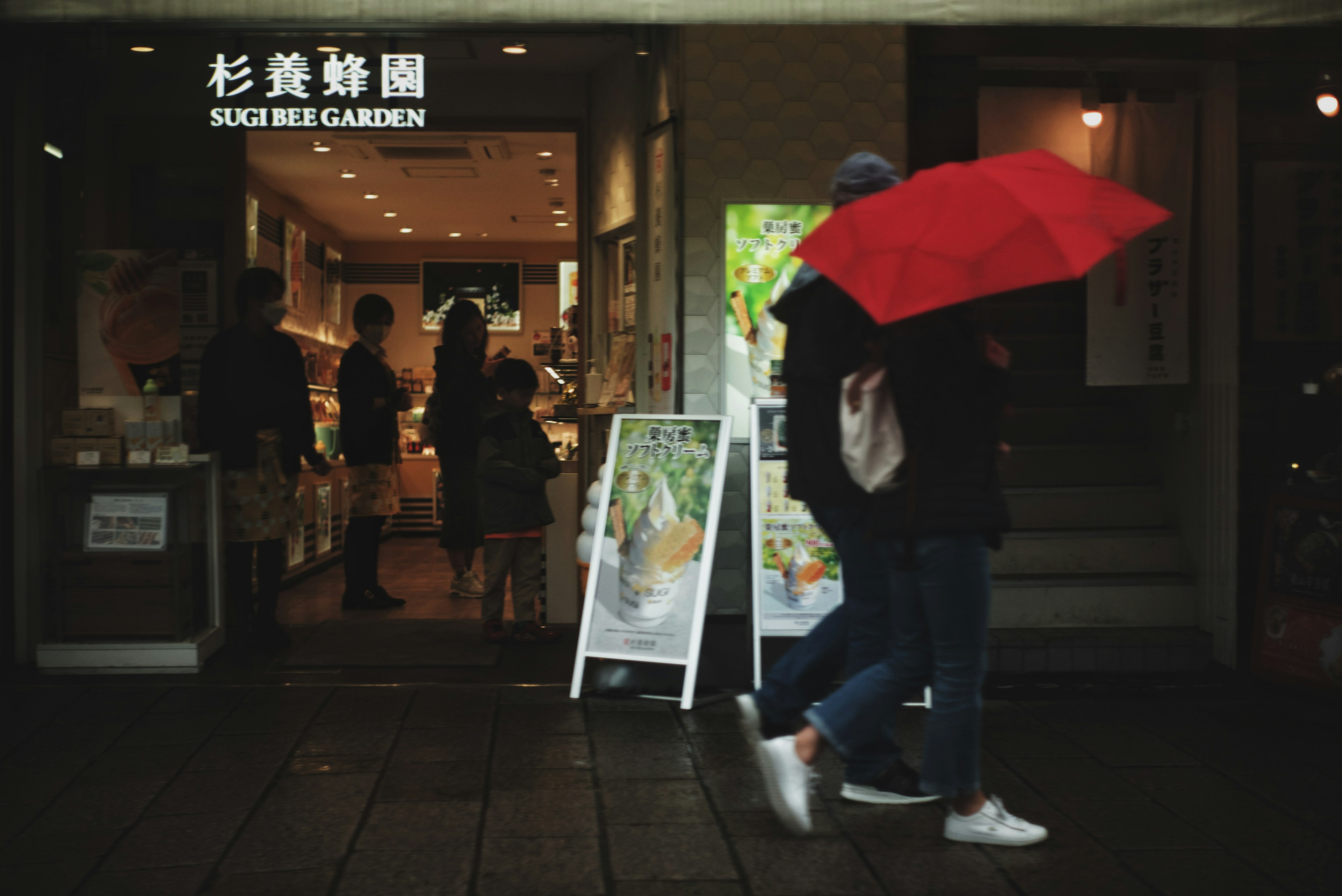 Personne tenant un parapluie rouge marchant devant un restaurant de sushi