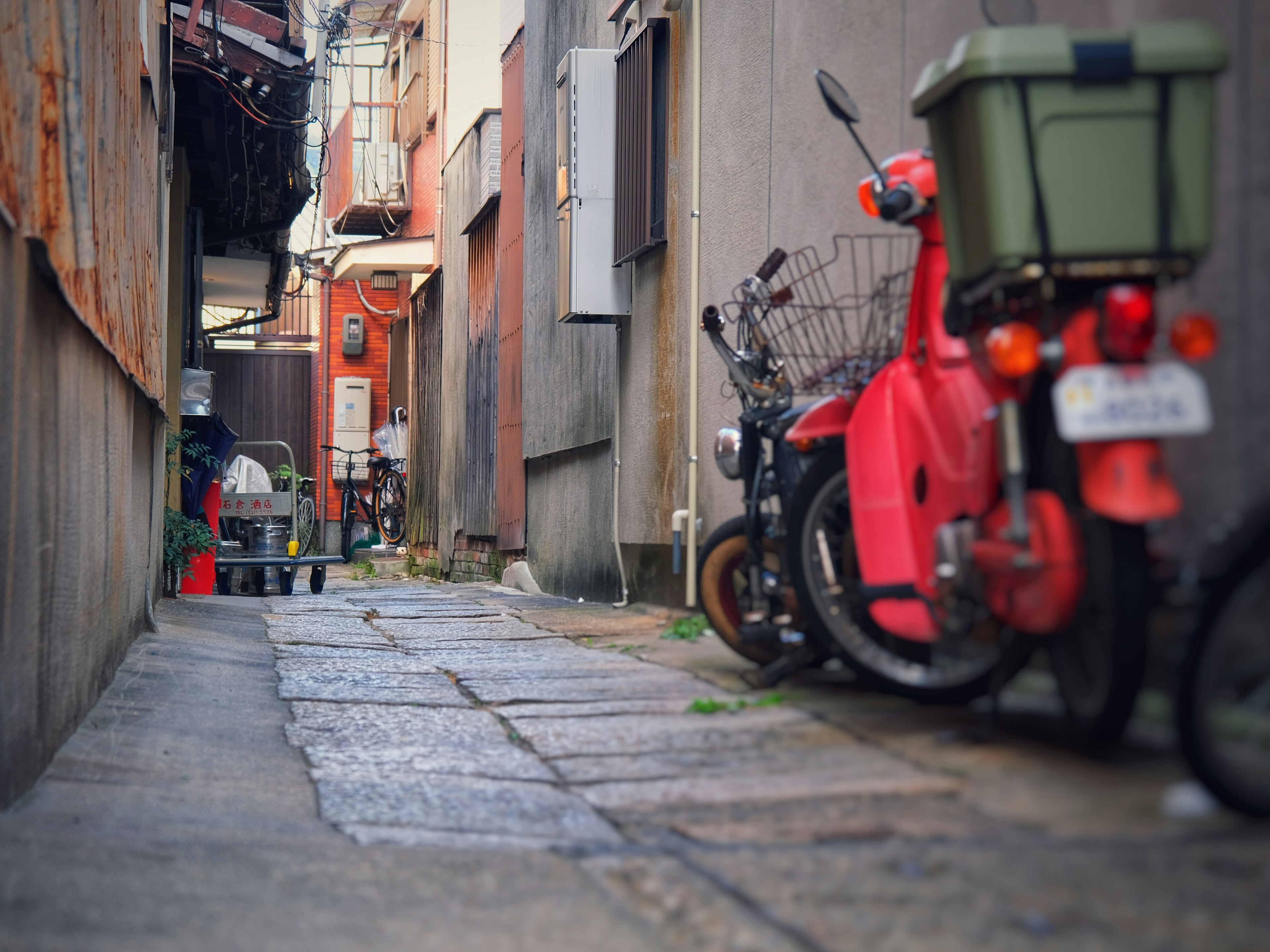 Narrow alley featuring parked red and green motorcycles with stone pavement