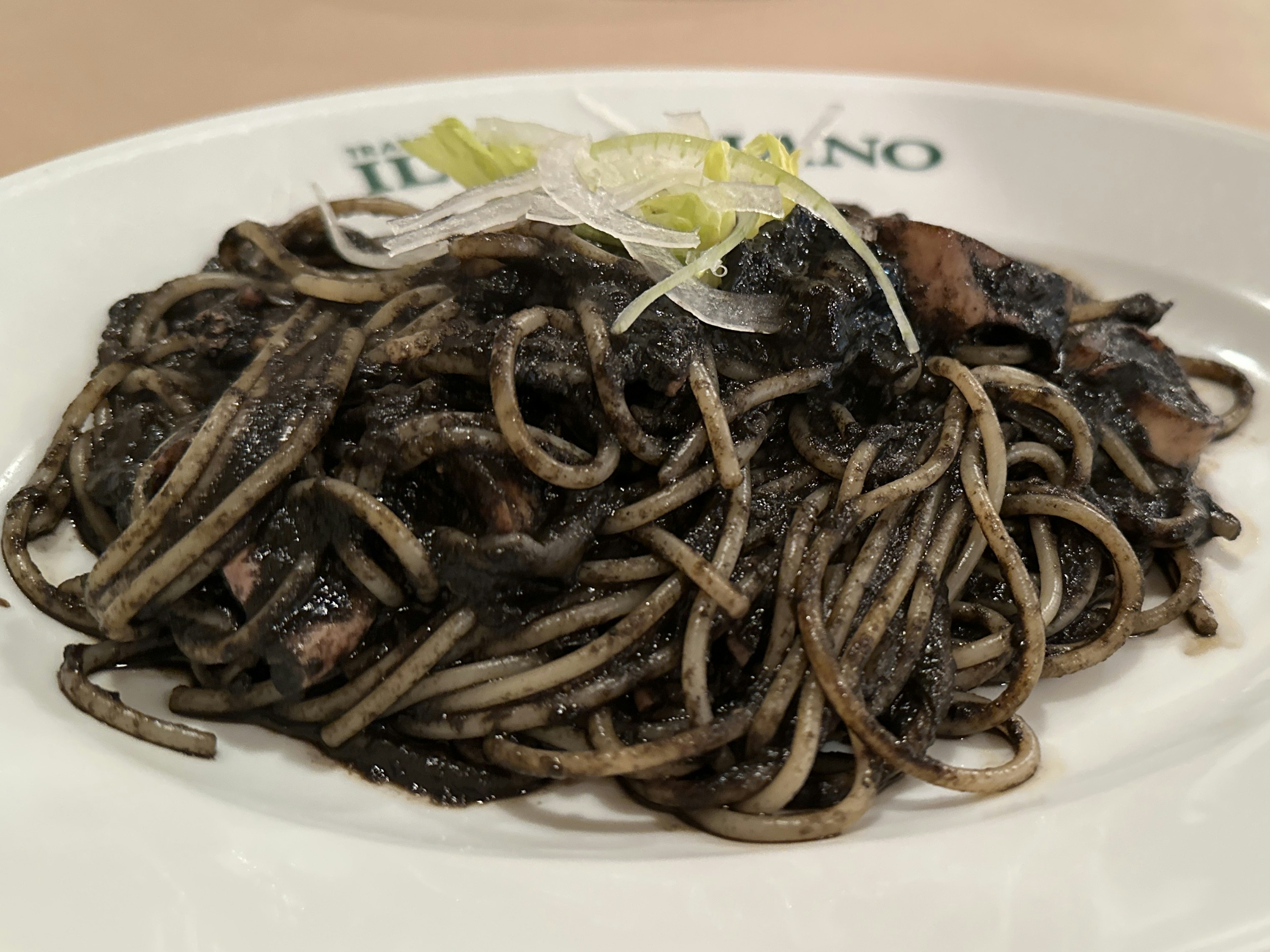 Piatto di spaghetti al nero di seppia guarnito con cipollotto