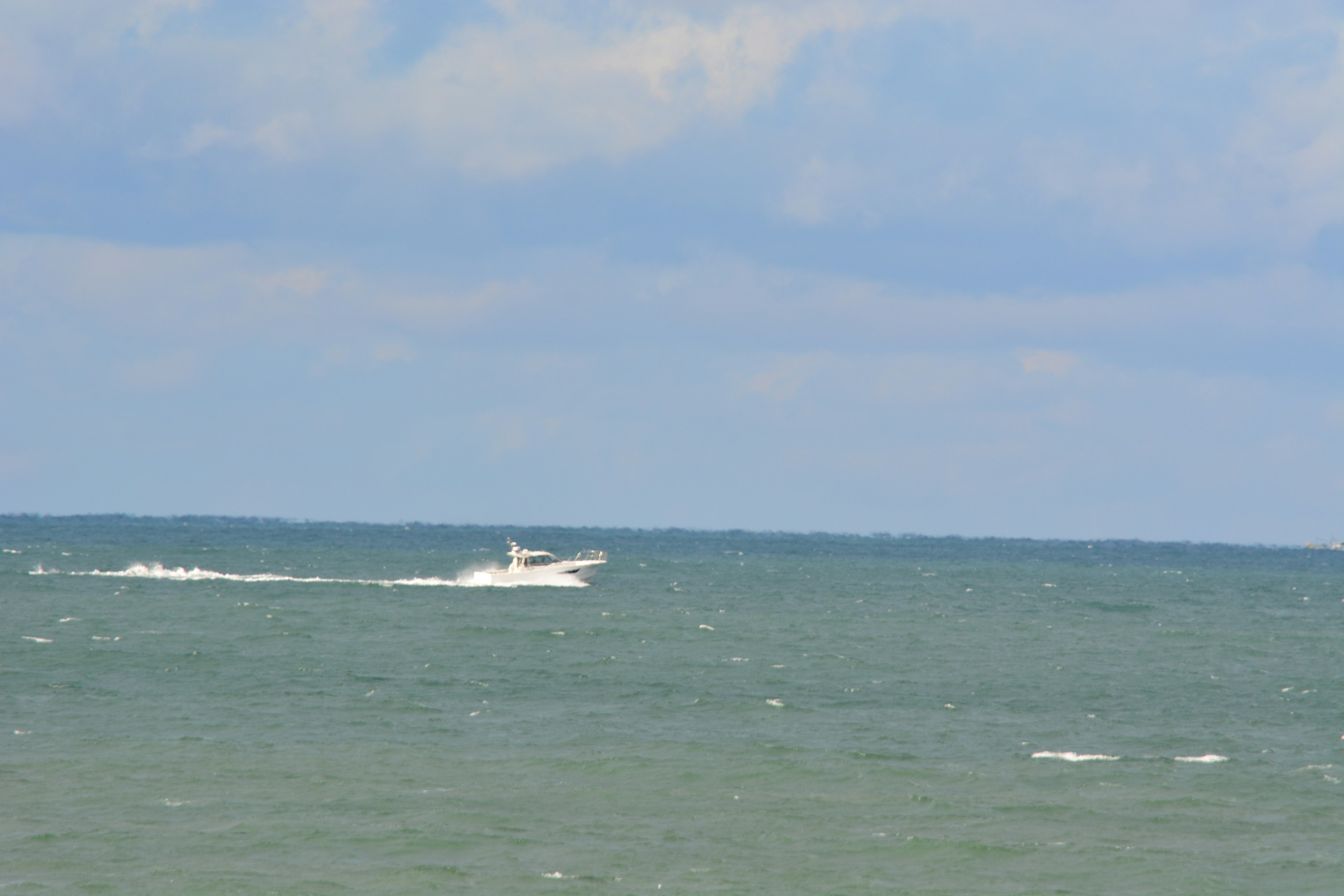 A white boat cruising on the sea under a blue sky