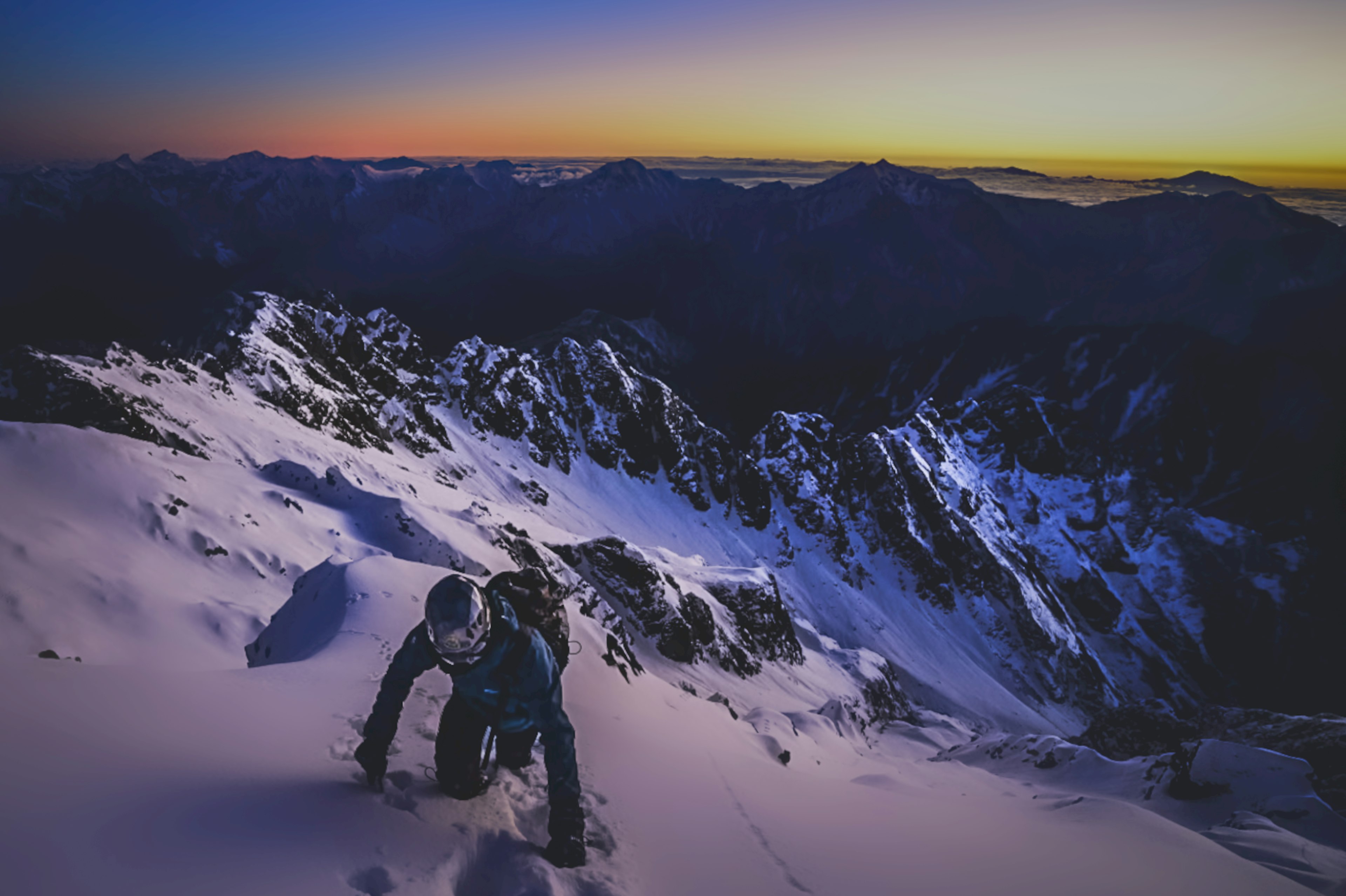 Silhouette of climber ascending a snow-covered mountain with a stunning sunset backdrop