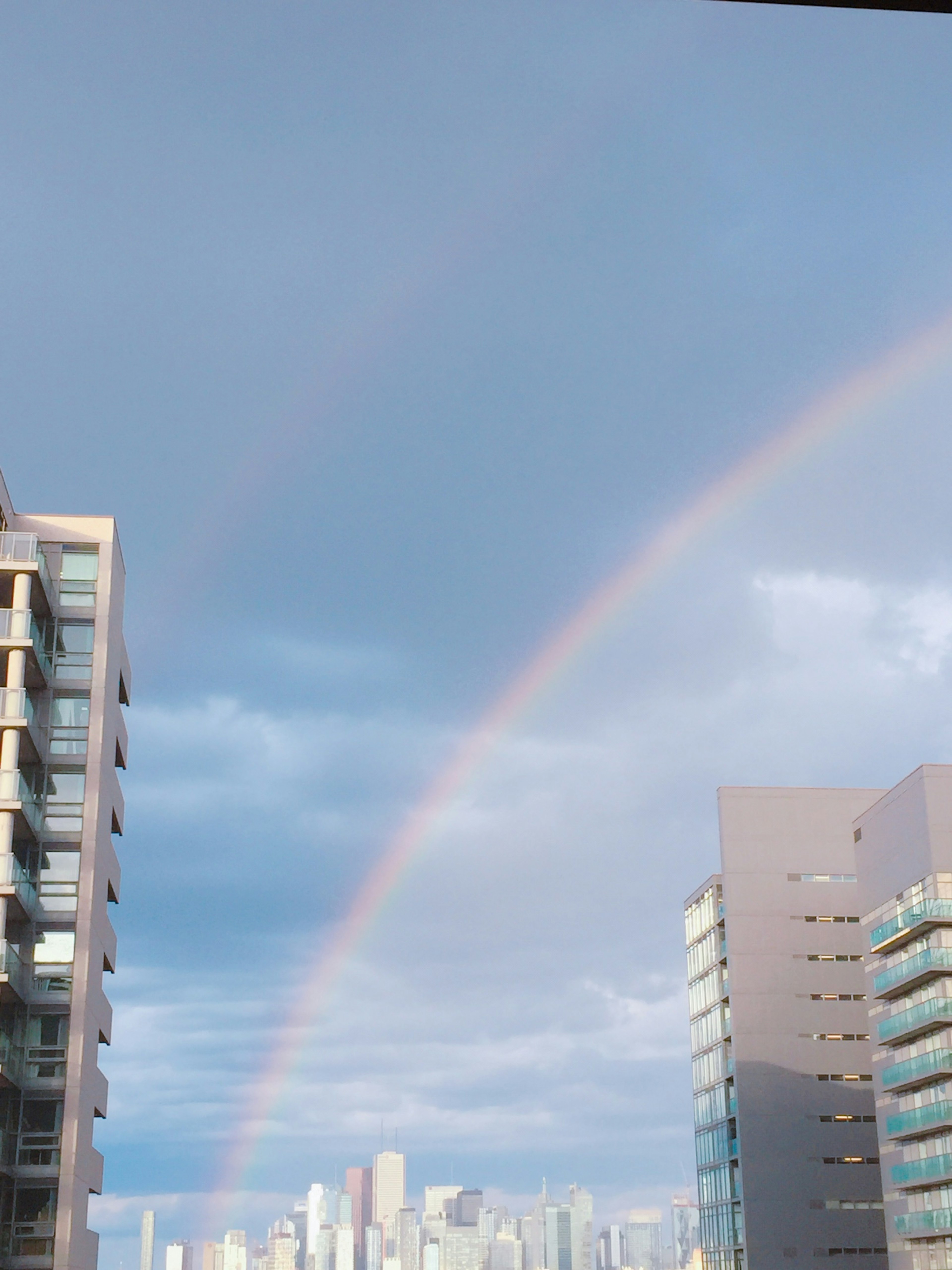 A rainbow arching between buildings under a cloudy sky