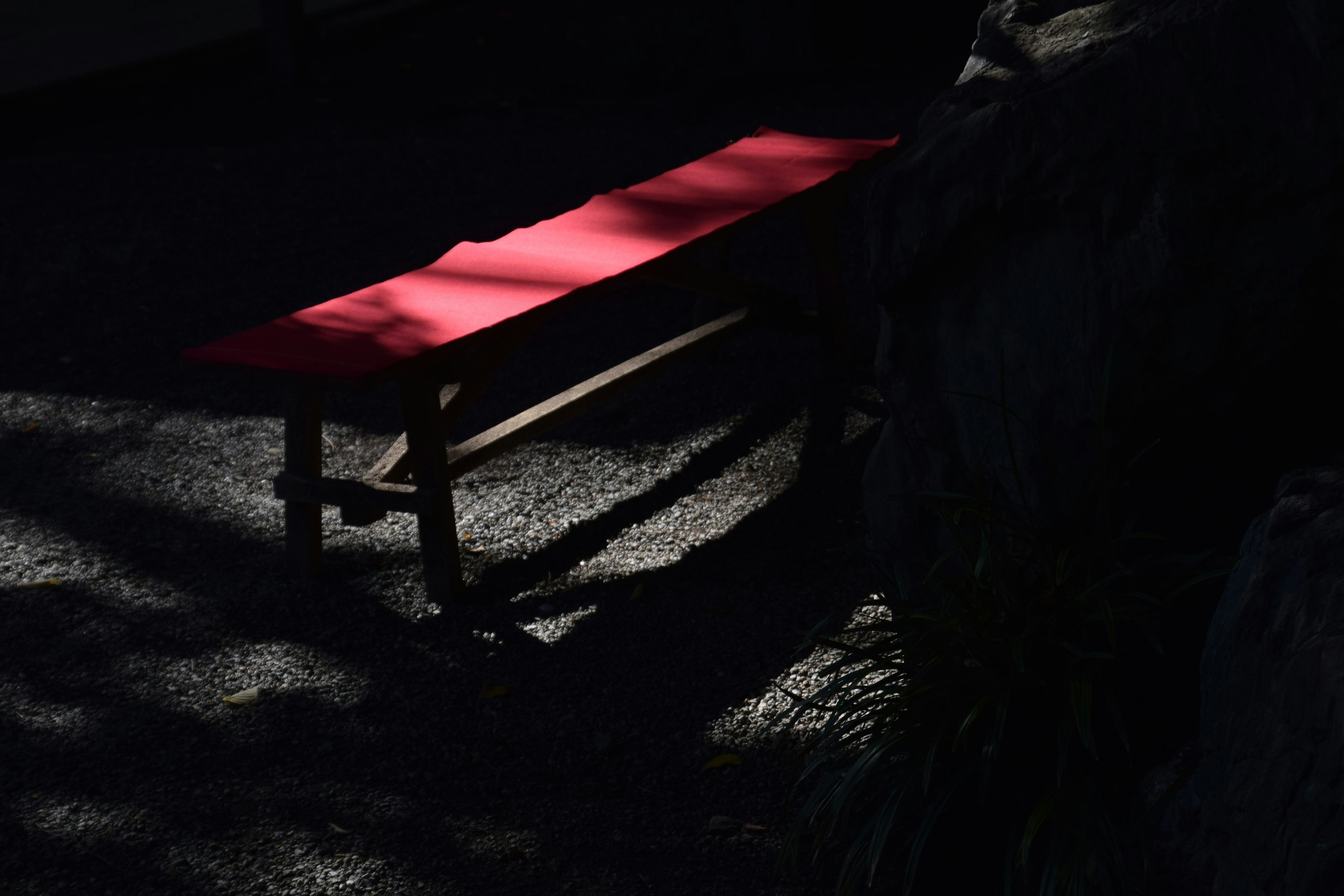 Eine rote Bank im Schatten auf einer strukturierten Oberfläche