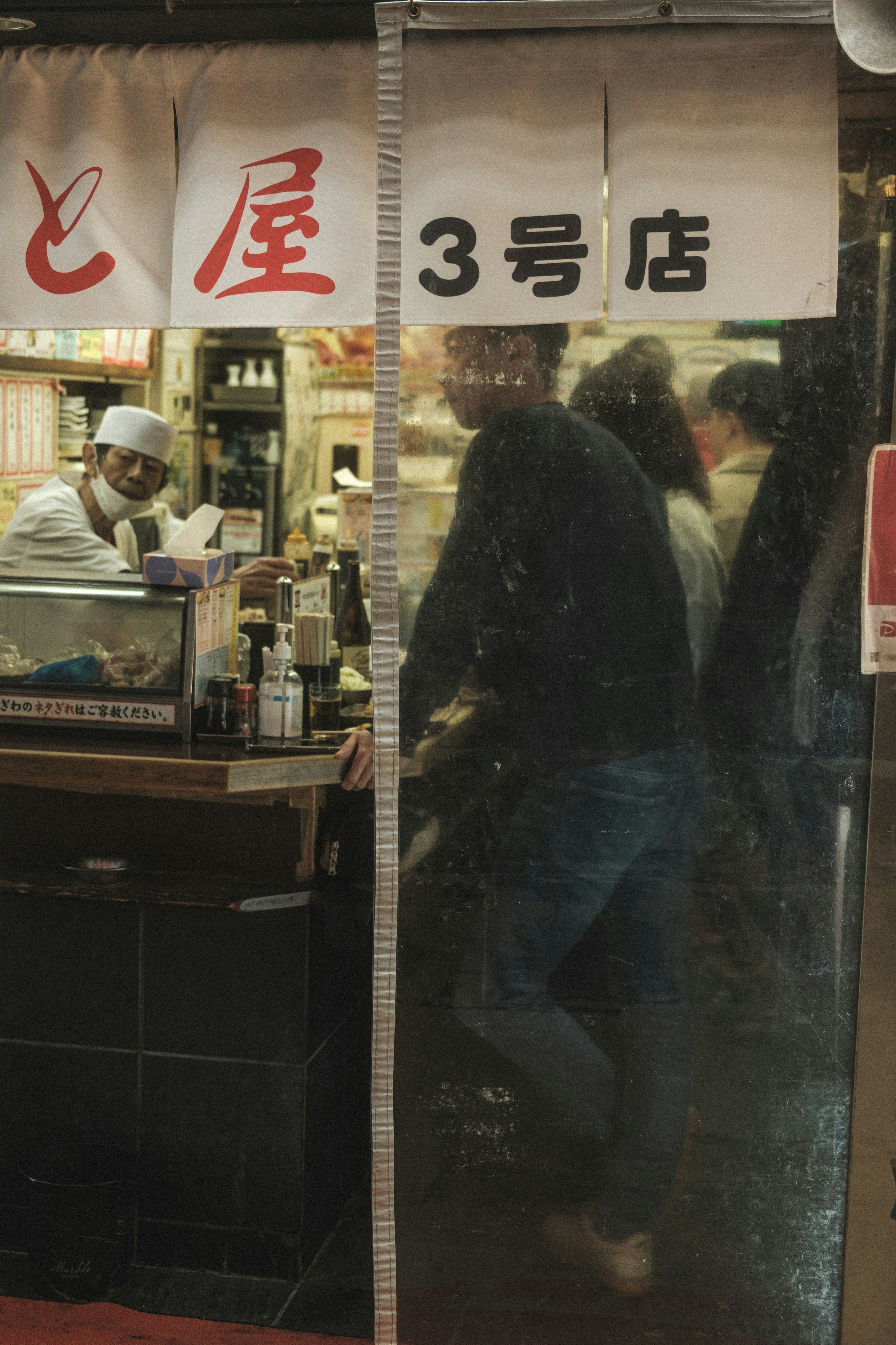 A glimpse through a clear plastic curtain showing people and the interior of a shop