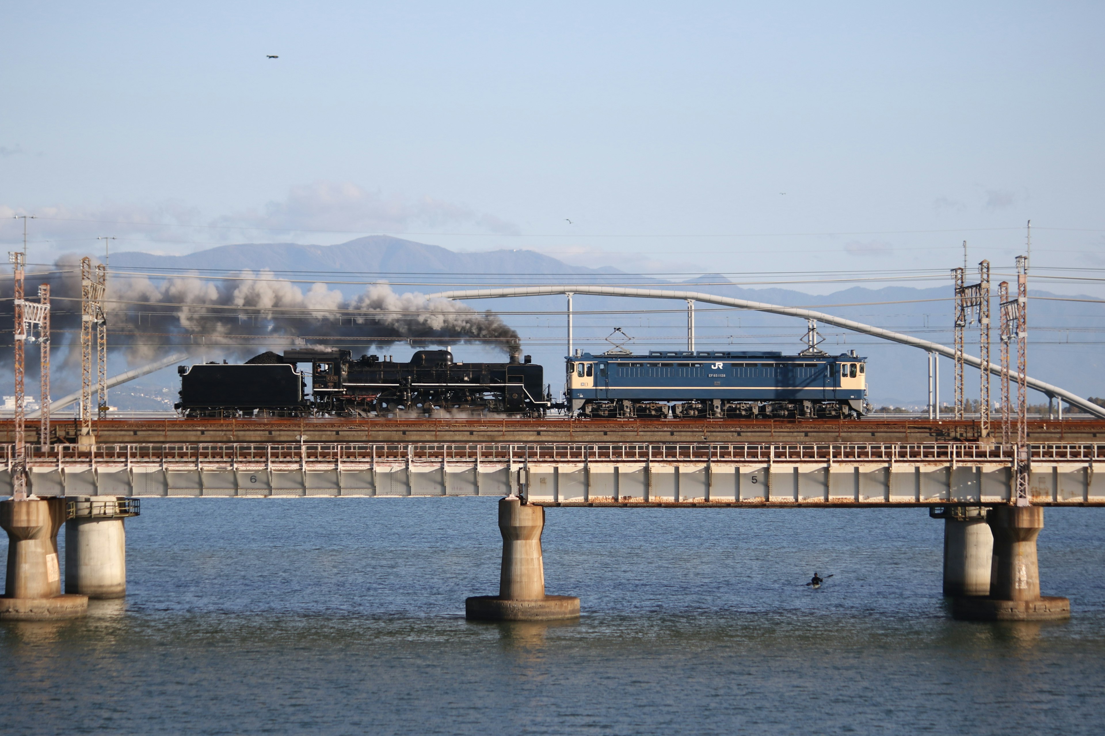 Steam locomotive and diesel locomotive crossing a bridge