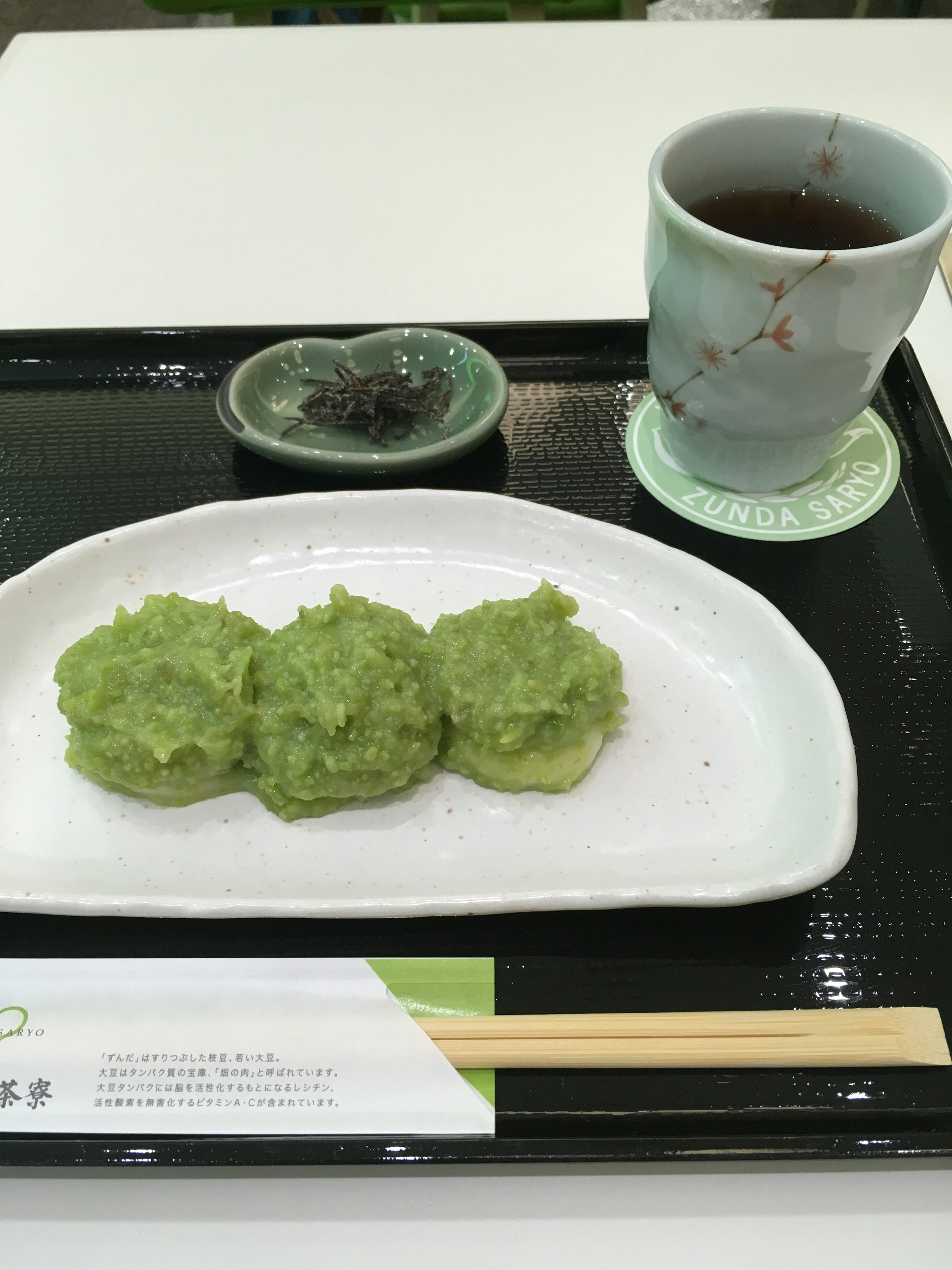 Three green Japanese sweets arranged on a plate with a cup of tea on a tray