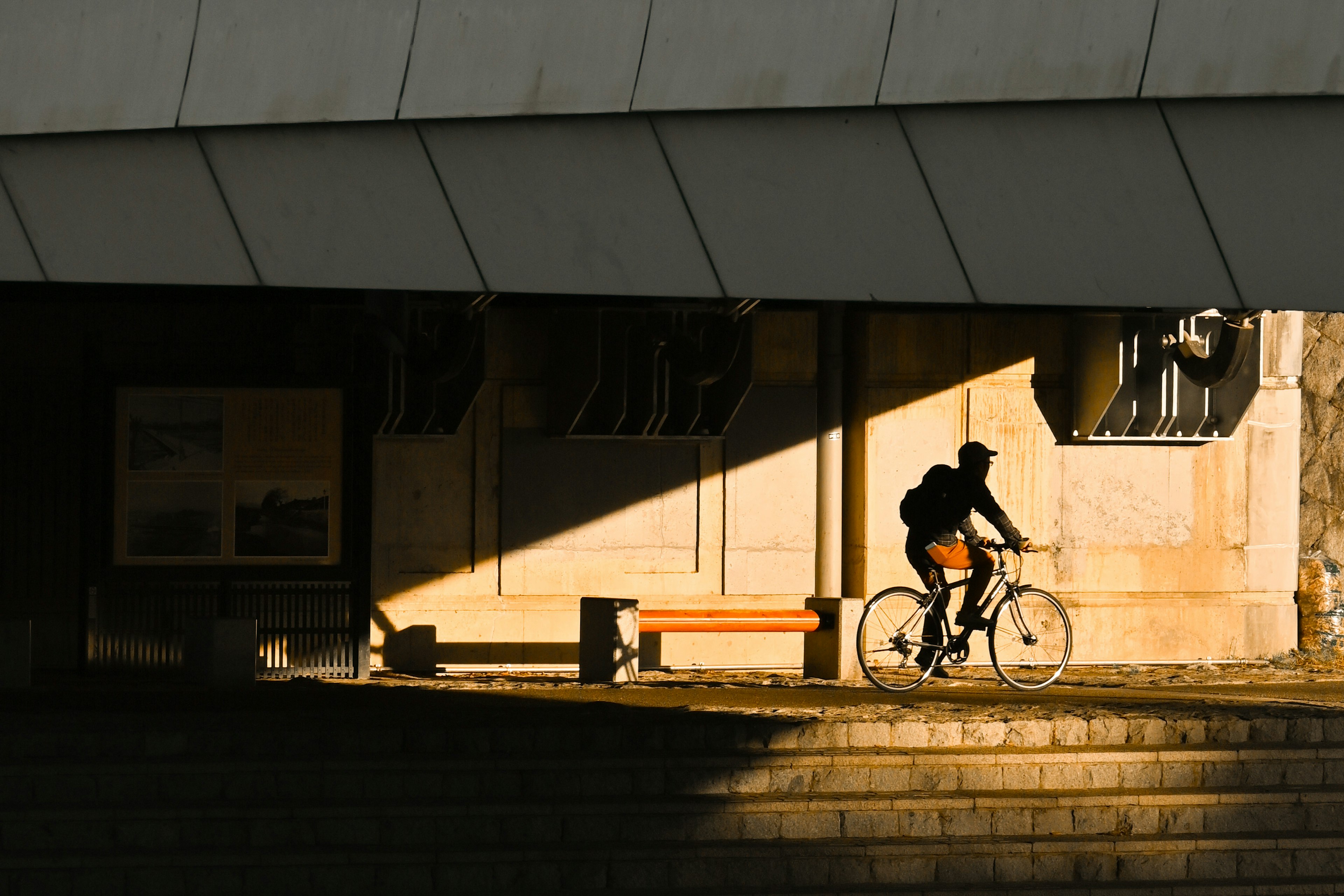 Silhouette of a cyclist riding under a building with geometric architecture during sunset