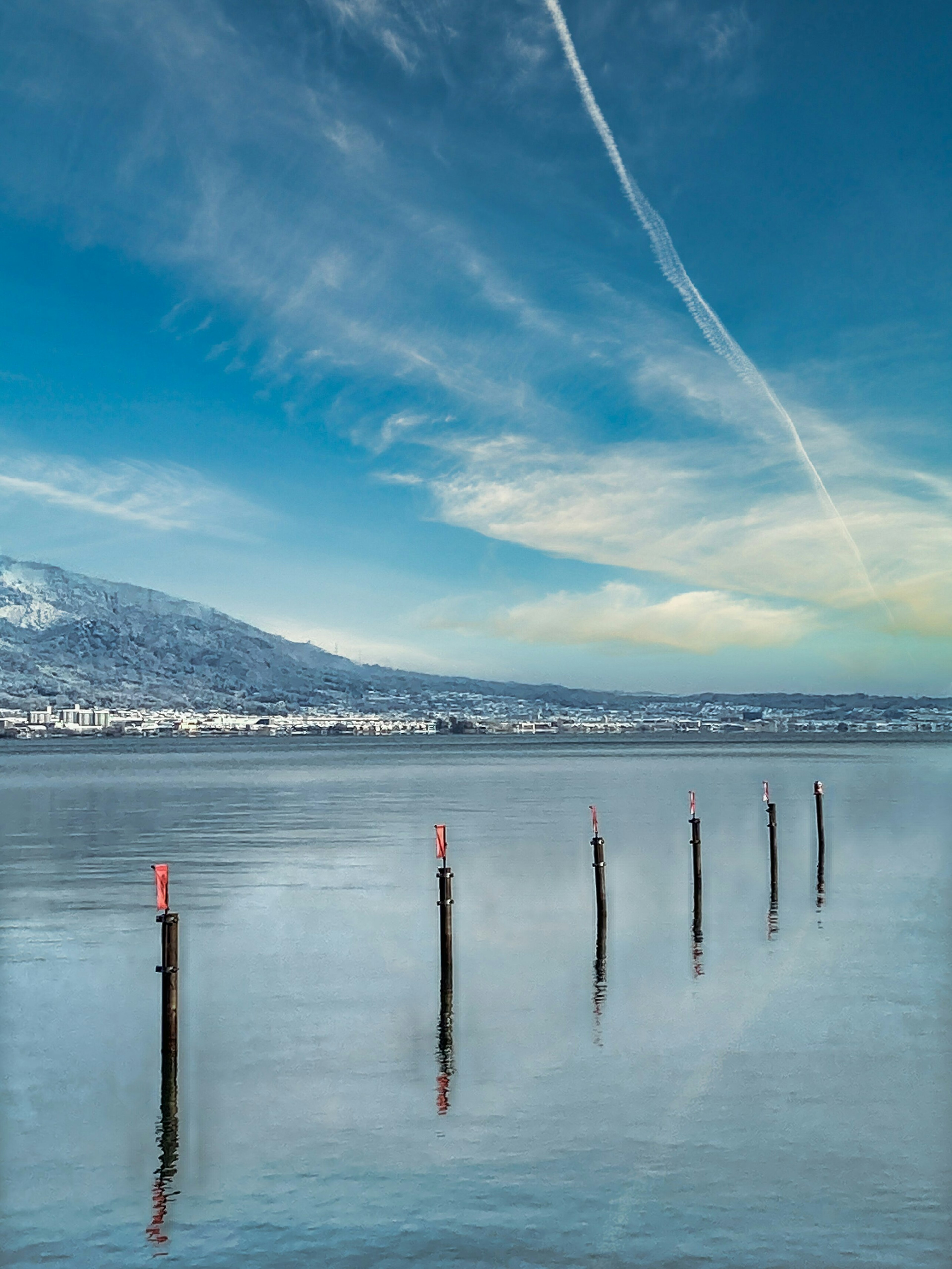 Calm water surface with red-marked posts and blue sky