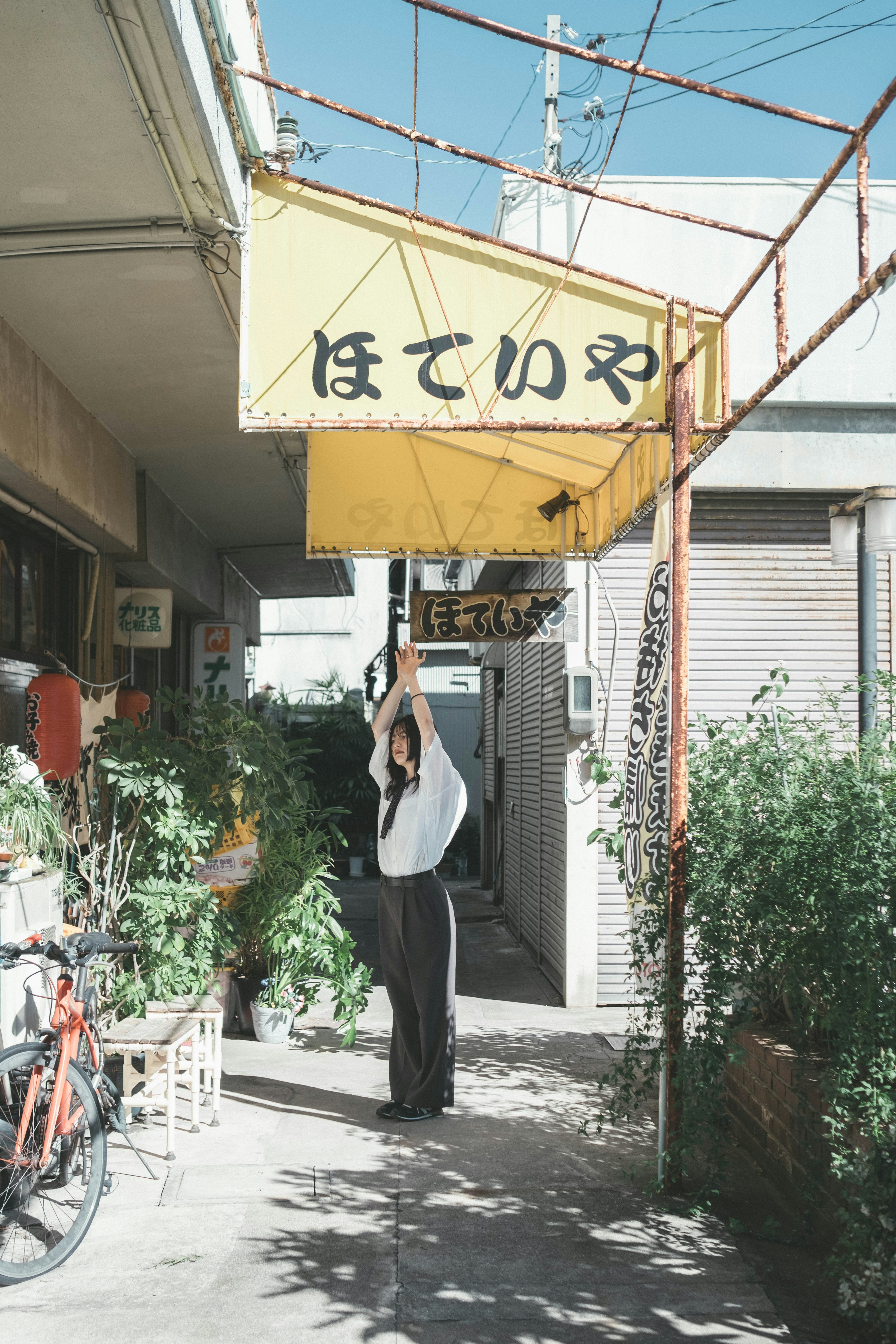 Person standing under a yellow sign with greenery in an alley