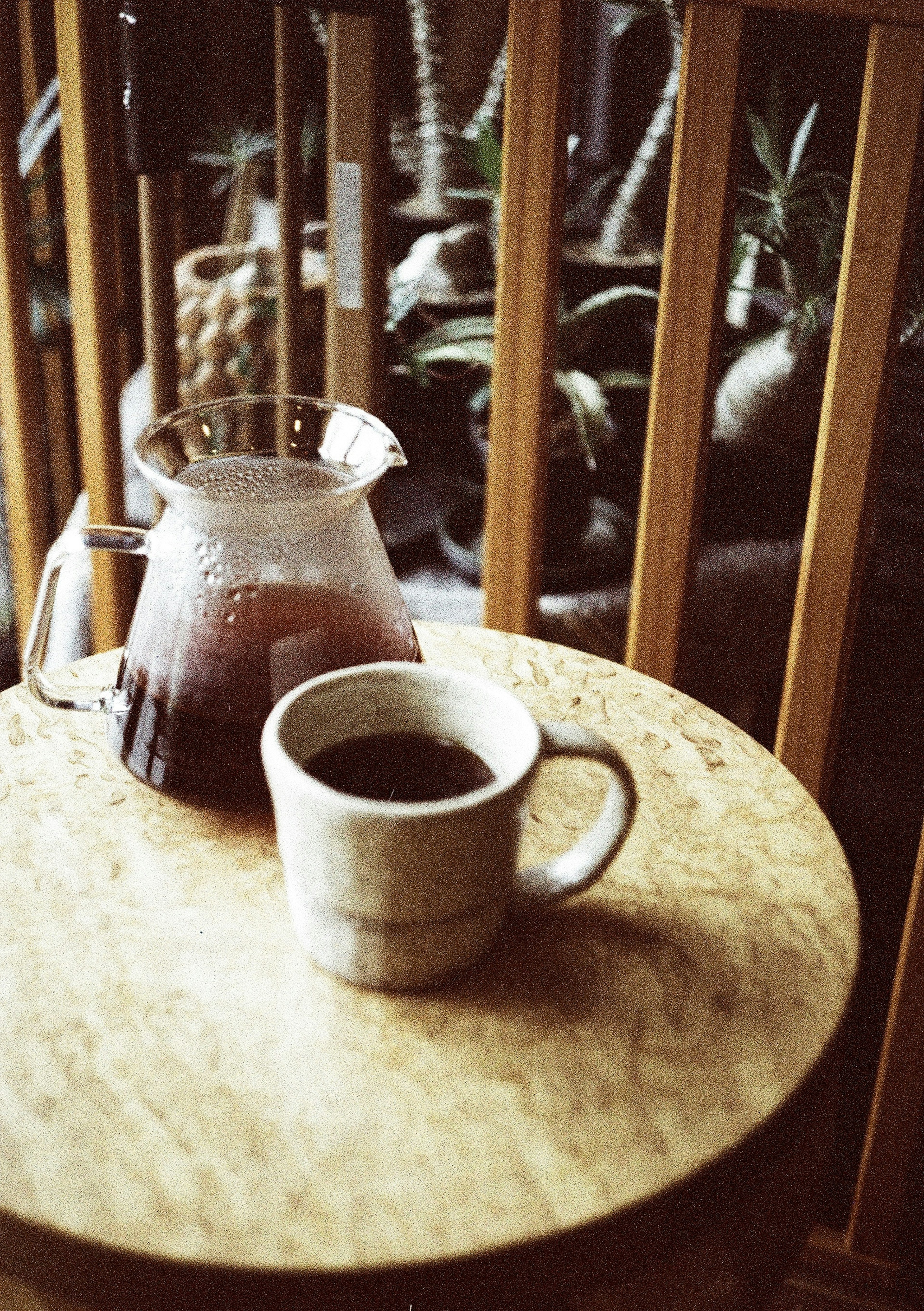 Cangkir kopi dan pitcher di atas meja dengan latar belakang kayu dan tanaman