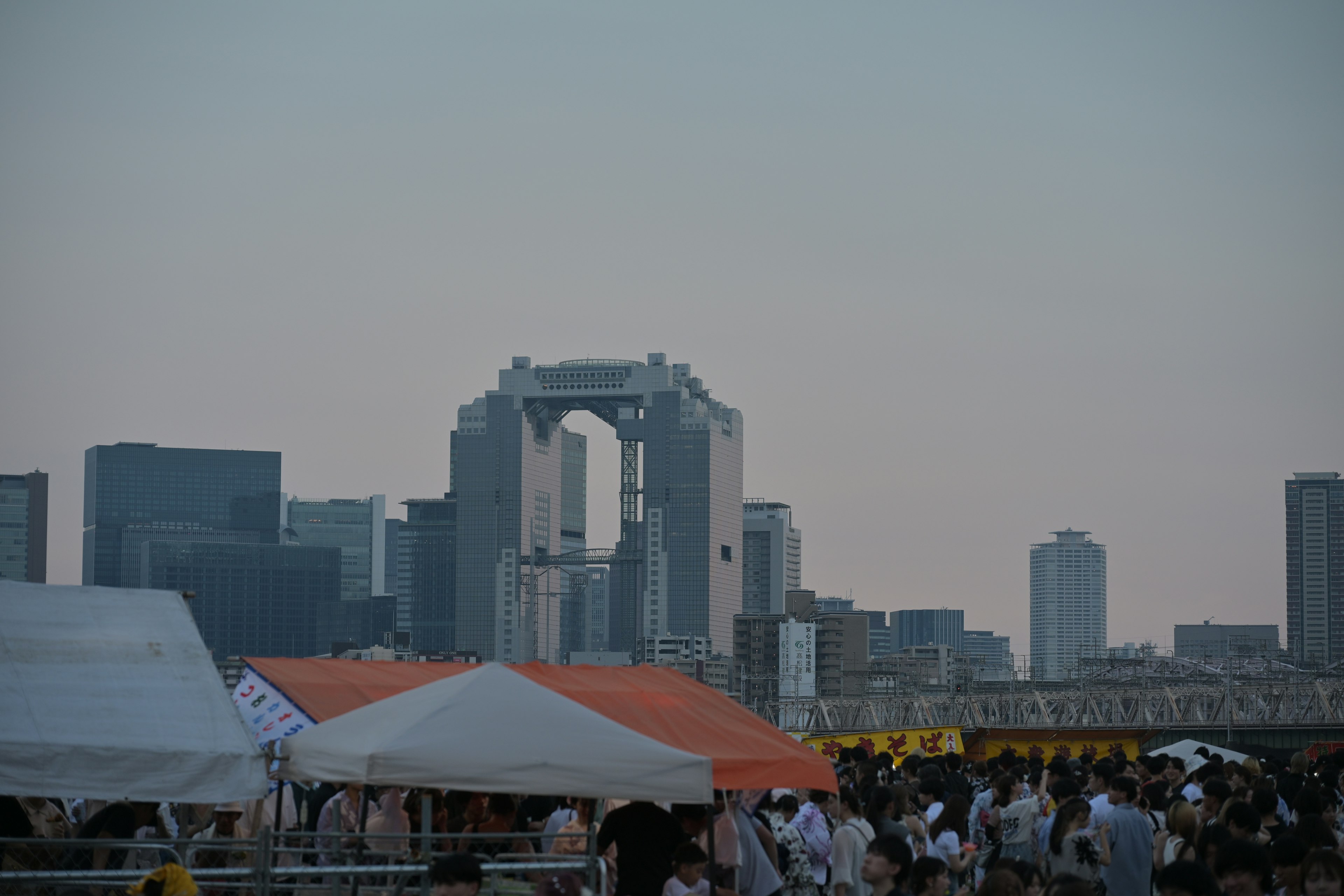 Urban skyline at dusk featuring the Unicorn Gundam statue and tents